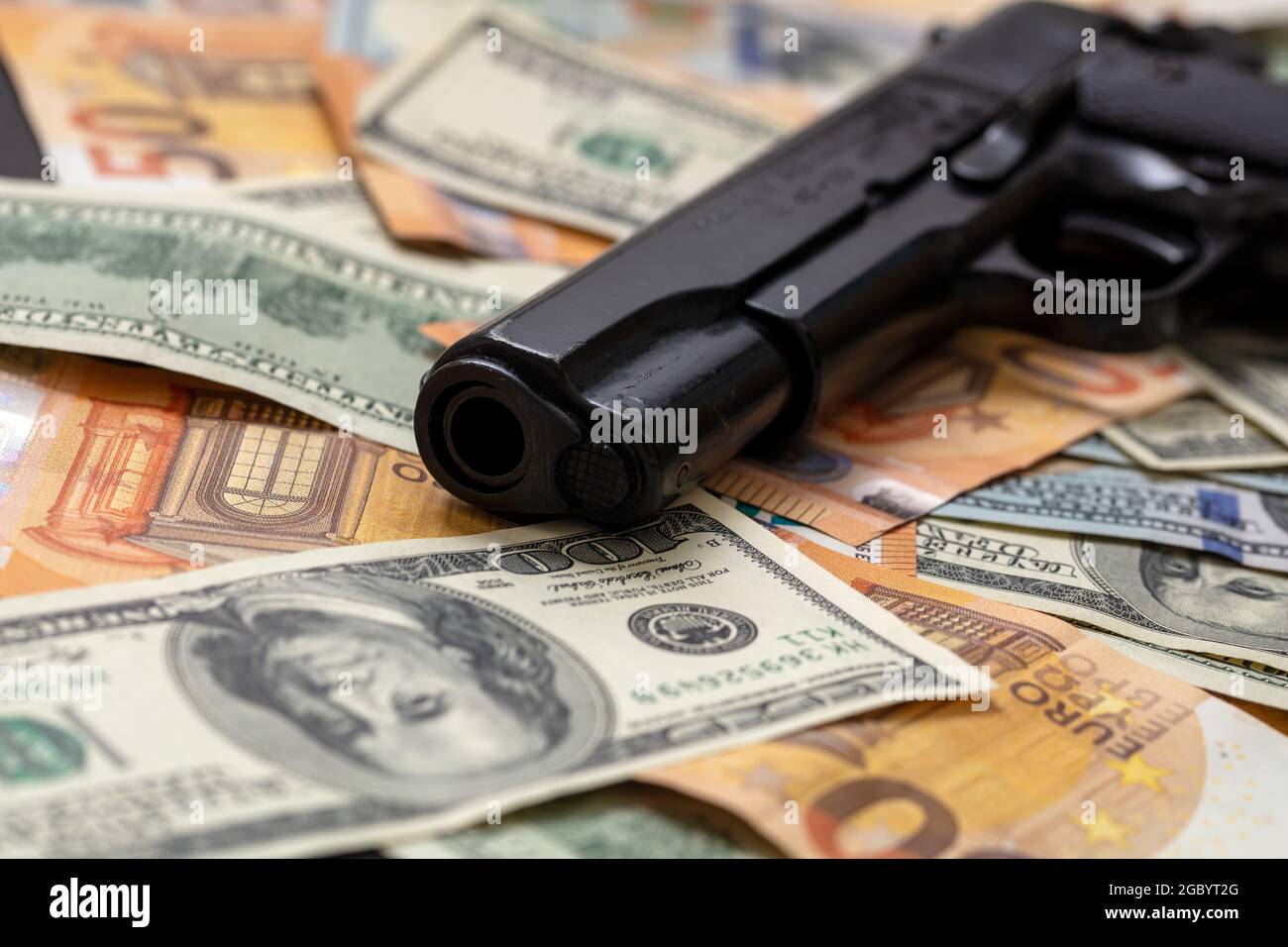 Pistola su fondo di banconote in dollari e in euro, vista closeup. Denaro criminale. Moneta nera e protezione, concetto di mafia e corruzione, Foto Stock