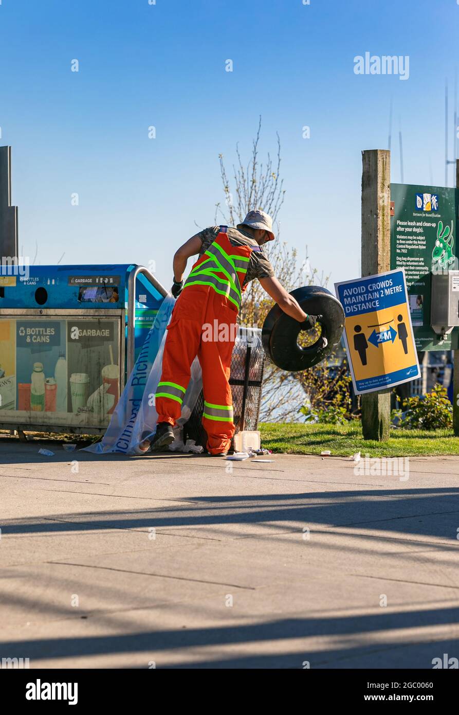 L'uomo di rimozione della spazzatura in uniforme che lavora per un'utilità pubblica che svuota i bidoni della spazzatura su una strada di un'area di Richmond, BC, Canada-Aprile 18,2021. Foto Stock