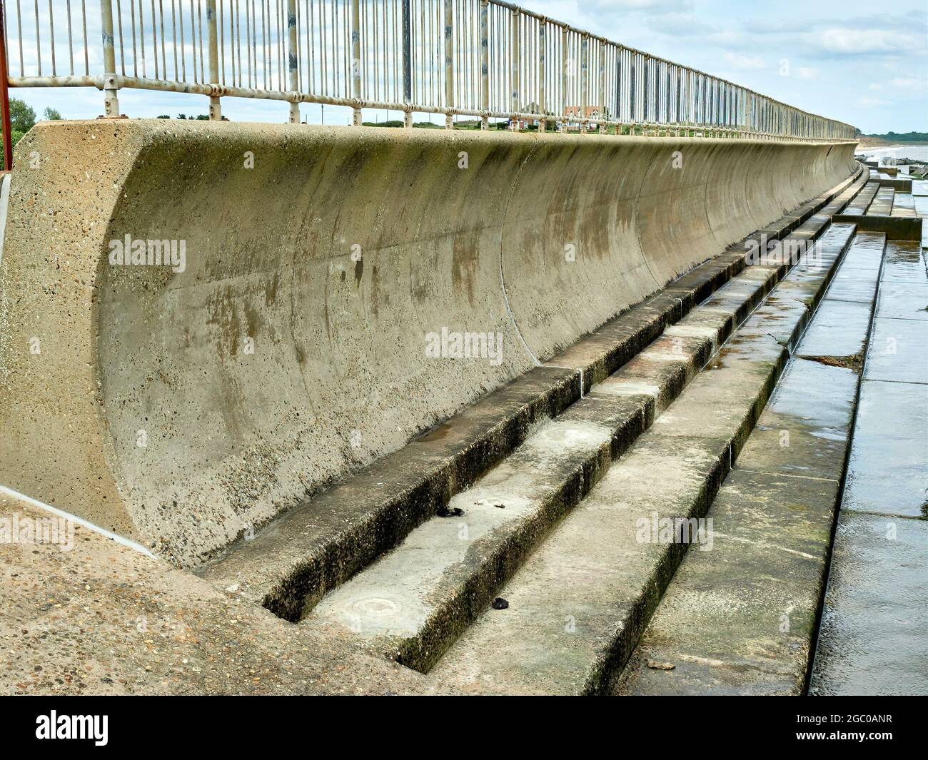 Vista verso il basso con l'estremità del muro di mare recurvato con base a gradini e barriera corrimano in alto. Foto Stock