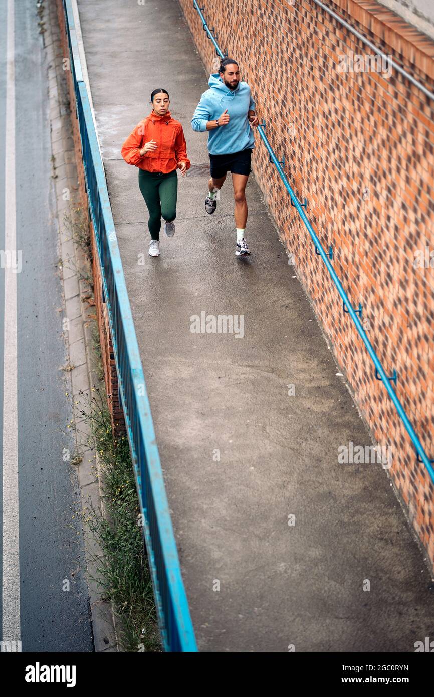 Giovani amici che indossano abiti sportivi che corrono all'aperto durante la giornata delle piogge. Sono concentrati e guardano davanti. Foto Stock