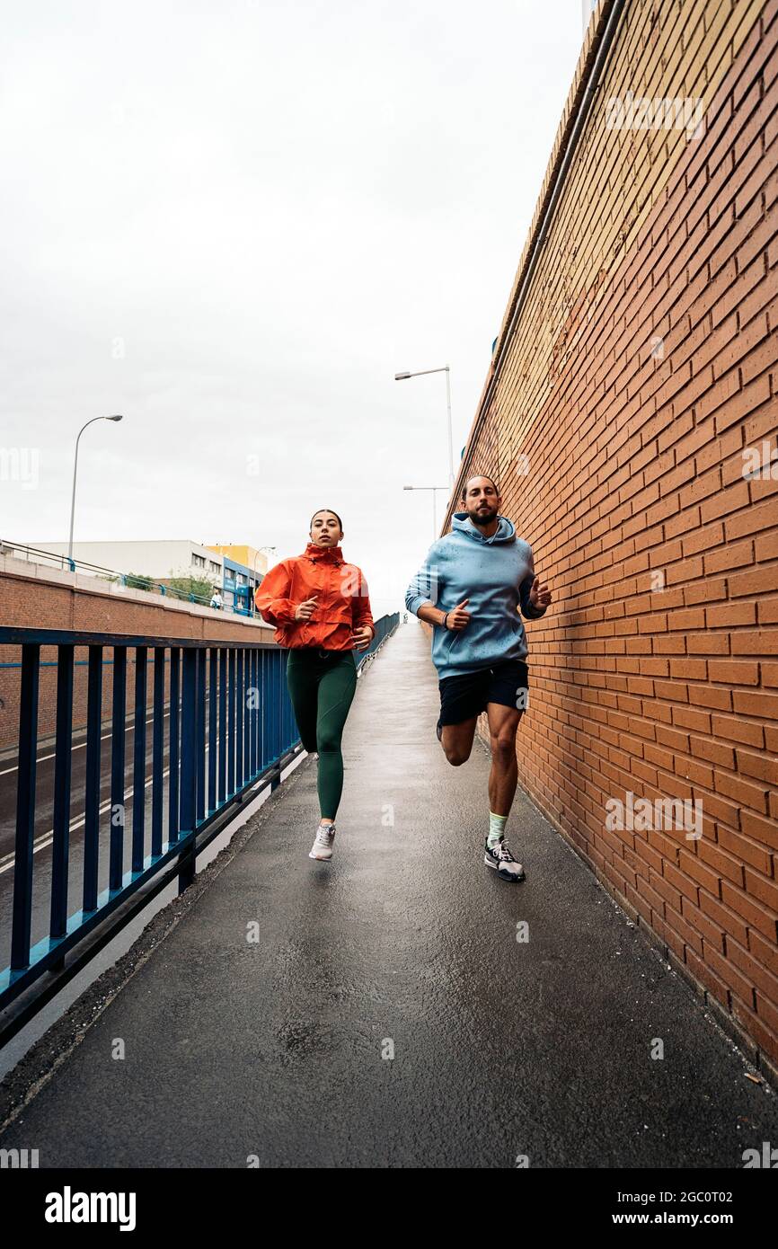 Giovani amici che indossano abiti sportivi che corrono all'aperto durante la giornata delle piogge. Sono concentrati e guardano davanti. Foto Stock