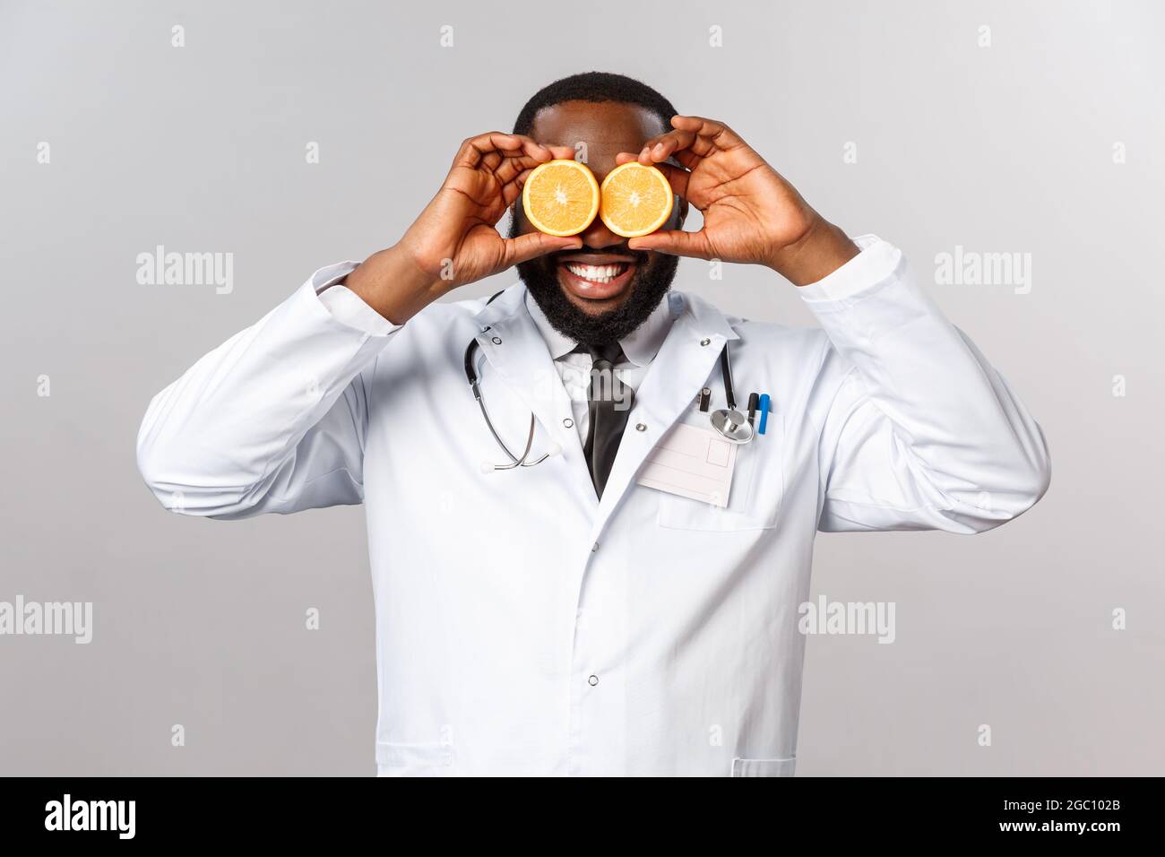 Salute, dieta sana e concetto di malattia. Felice divertente medico afroamericano maschio in camice bianco, aumentare l'umore di capretto sdraiato in infermeria, spiegare Foto Stock