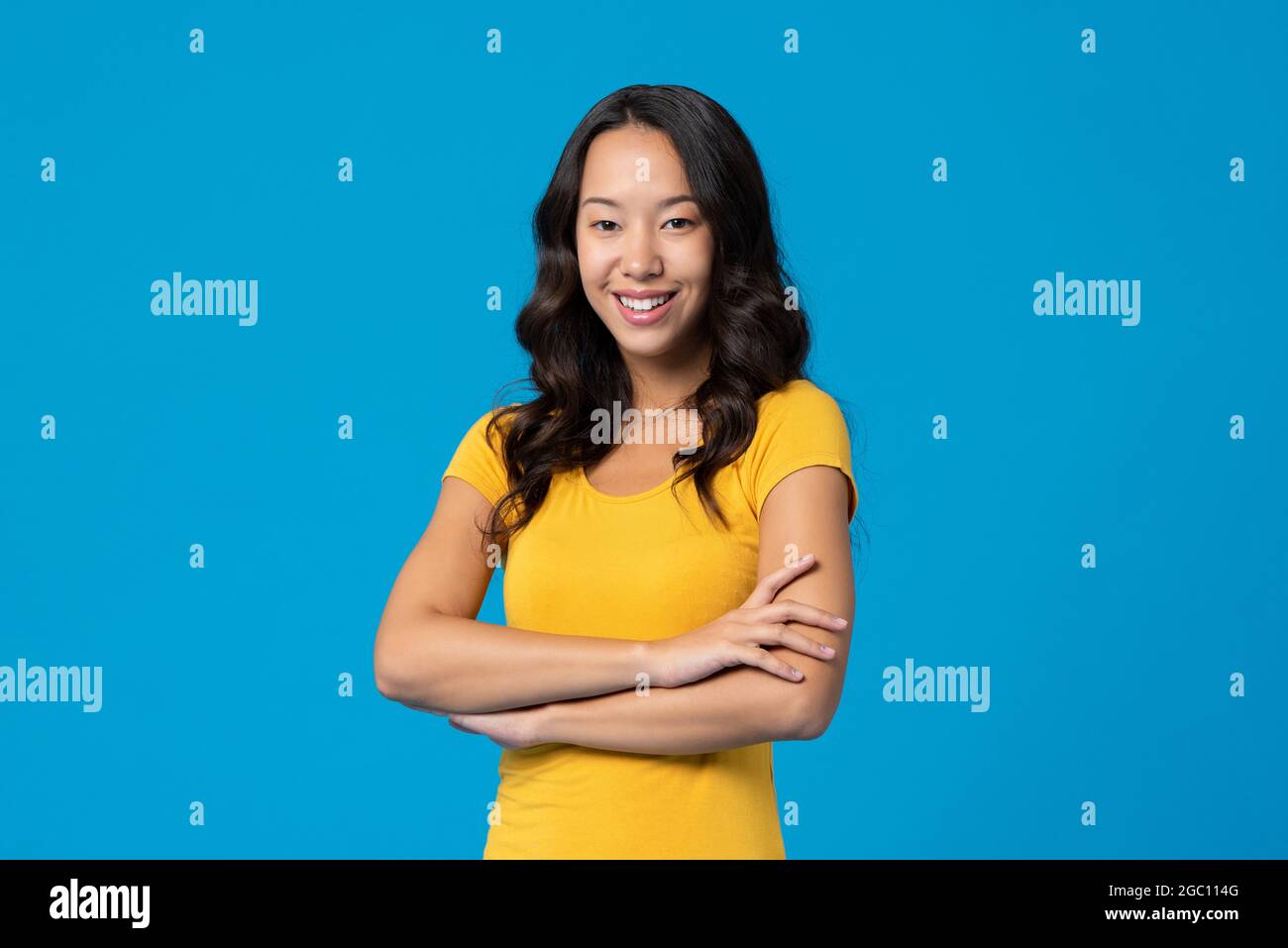 Sorridente felice gara mista giovane donna millenaria con le braccia incrociate isolato su sfondo blu studio Foto Stock