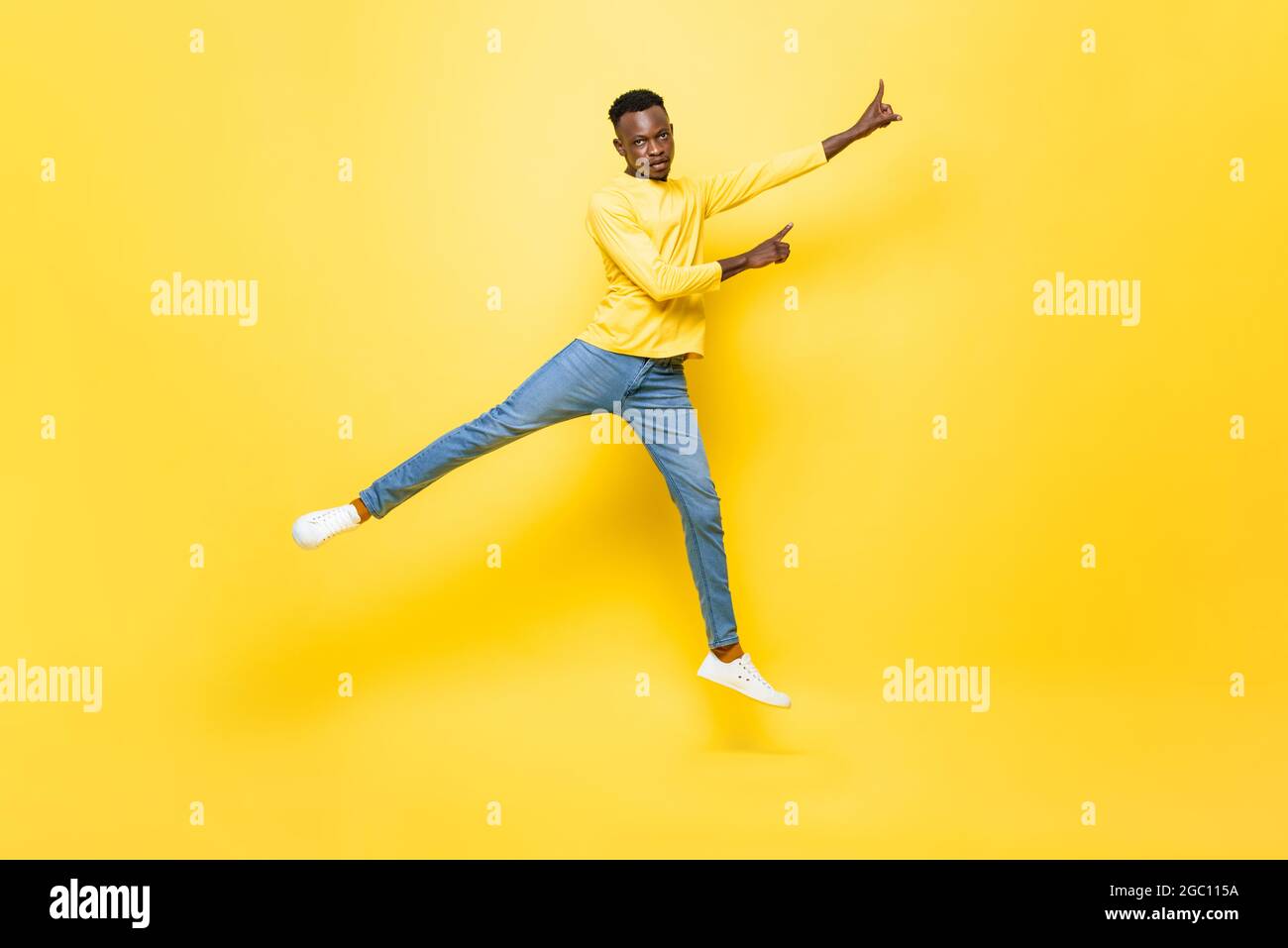 Giovane uomo africano energico saltando e puntando mani su isolato sfondo giallo studio Foto Stock