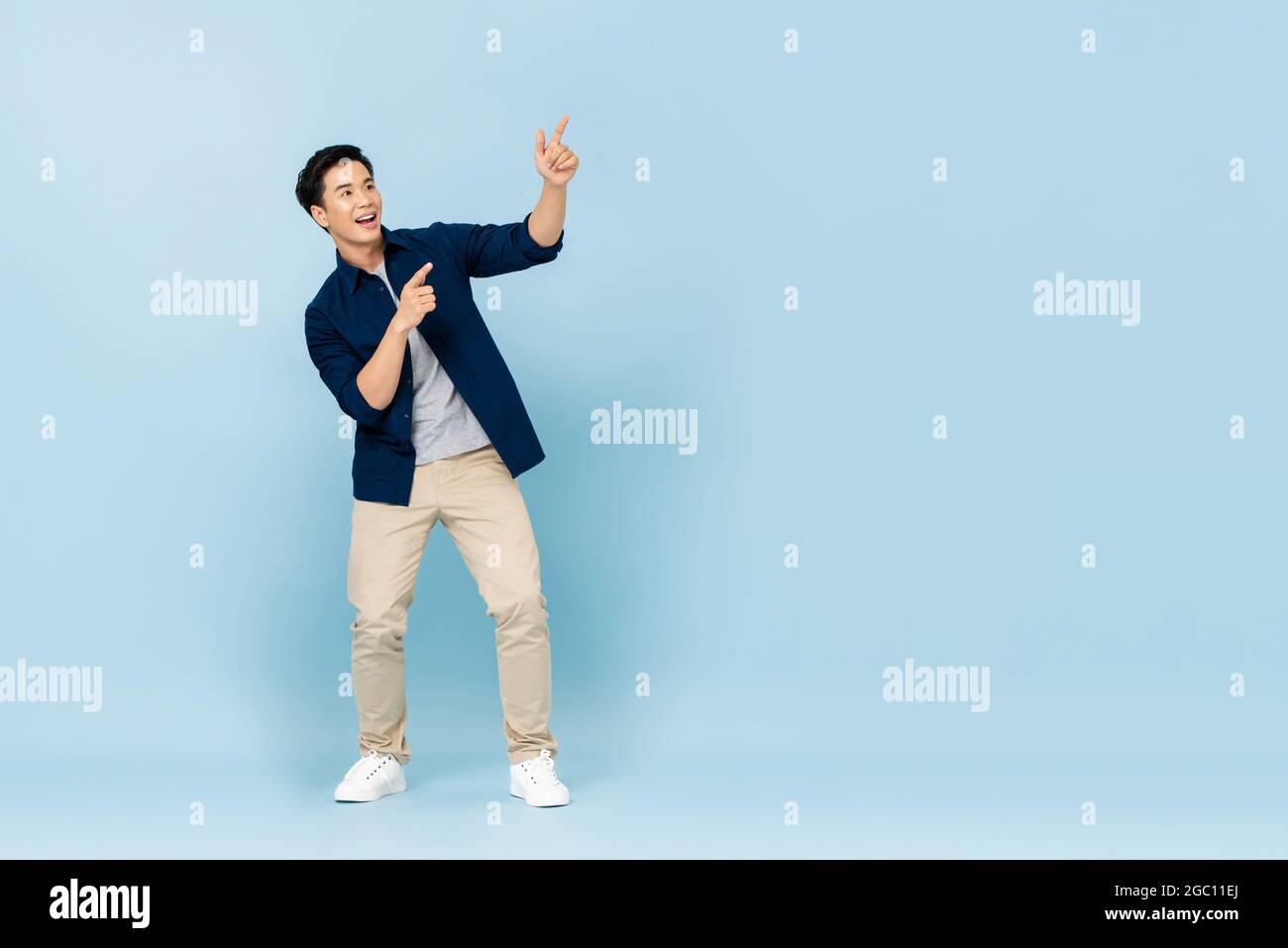Ritratto a lunghezza intera di sorridente giovane bell'uomo asiatico che punta le dita verso lo spazio vuoto da parte in studio isolato sfondo azzurro Foto Stock