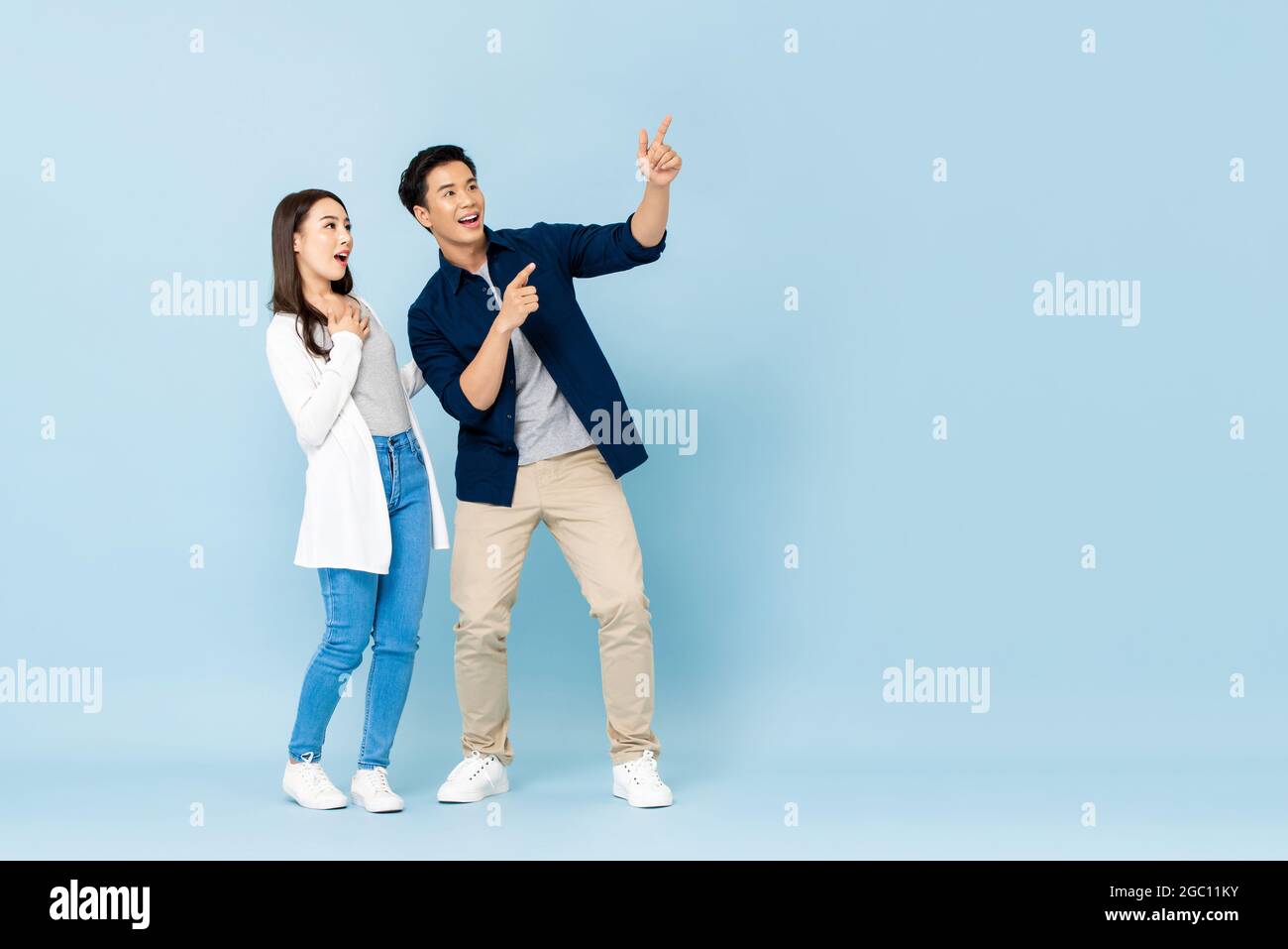 Ritratto a lunghezza intera di felici eccitati turisti asiatici coppia indicando le mani a spazio vuoto su isolato sfondo azzurro Foto Stock