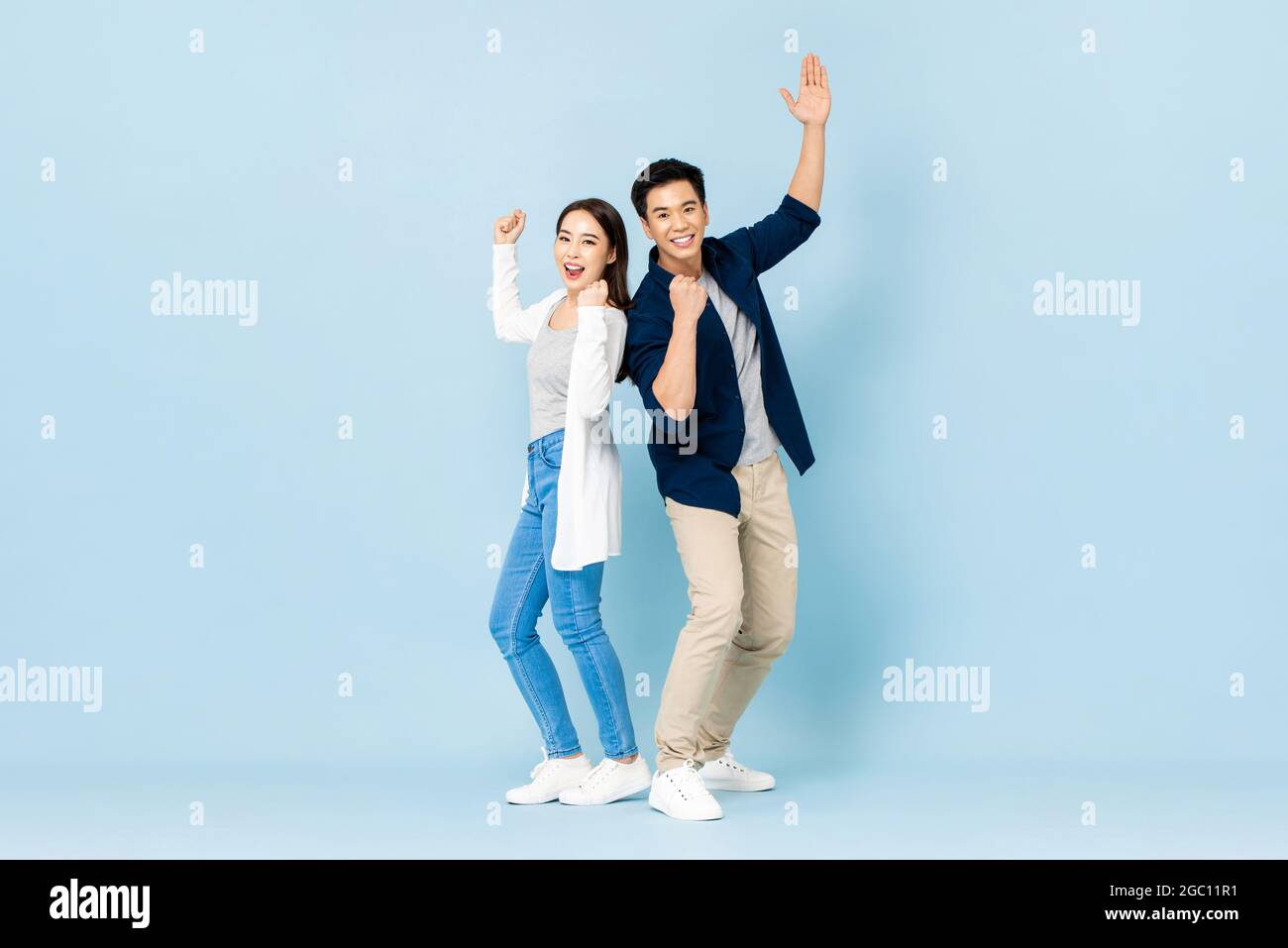 Ritratto a lunghezza intera di allegra coppia asiatica in piedi indietro sorridente e clenching pugni in blu chiaro isolato sfondo studio Foto Stock