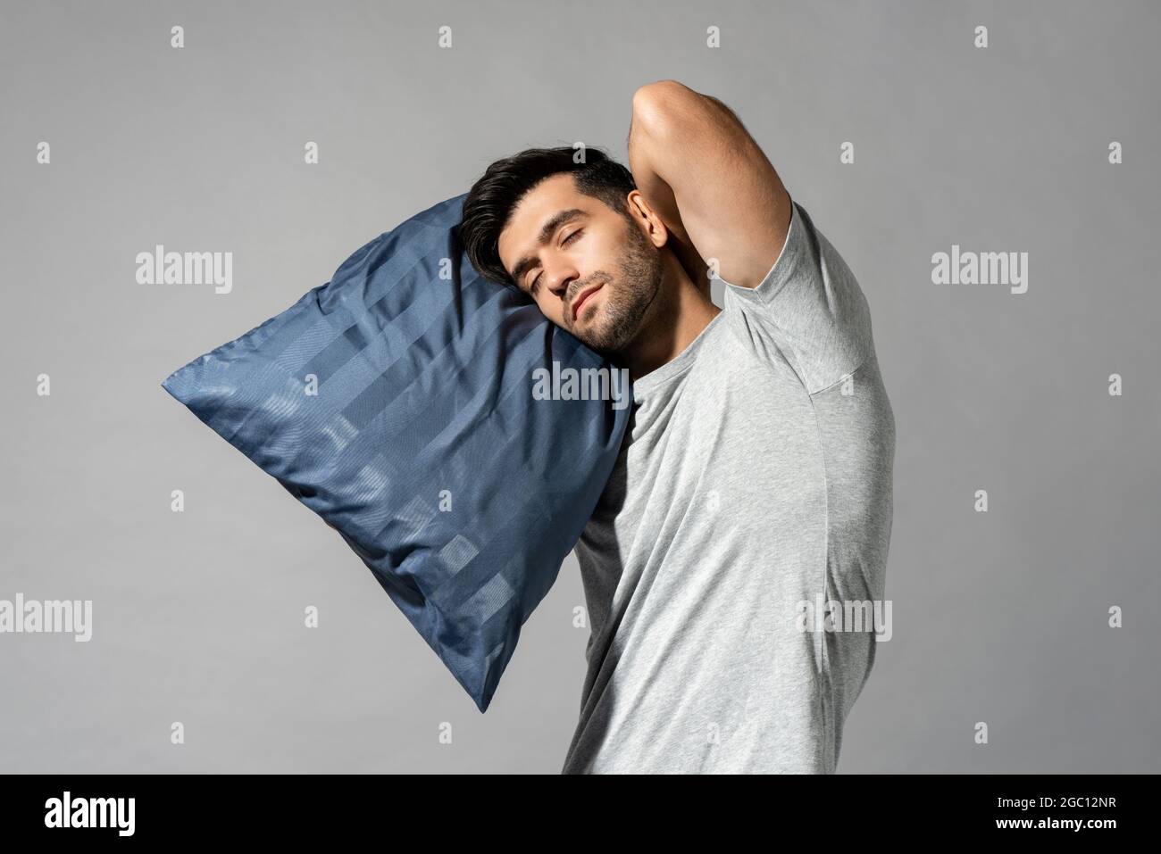 Giovane addormentato che tiene il suo cuscino in piedi in grigio chiaro isolato sfondo studio, sleepwalking concetto Foto Stock