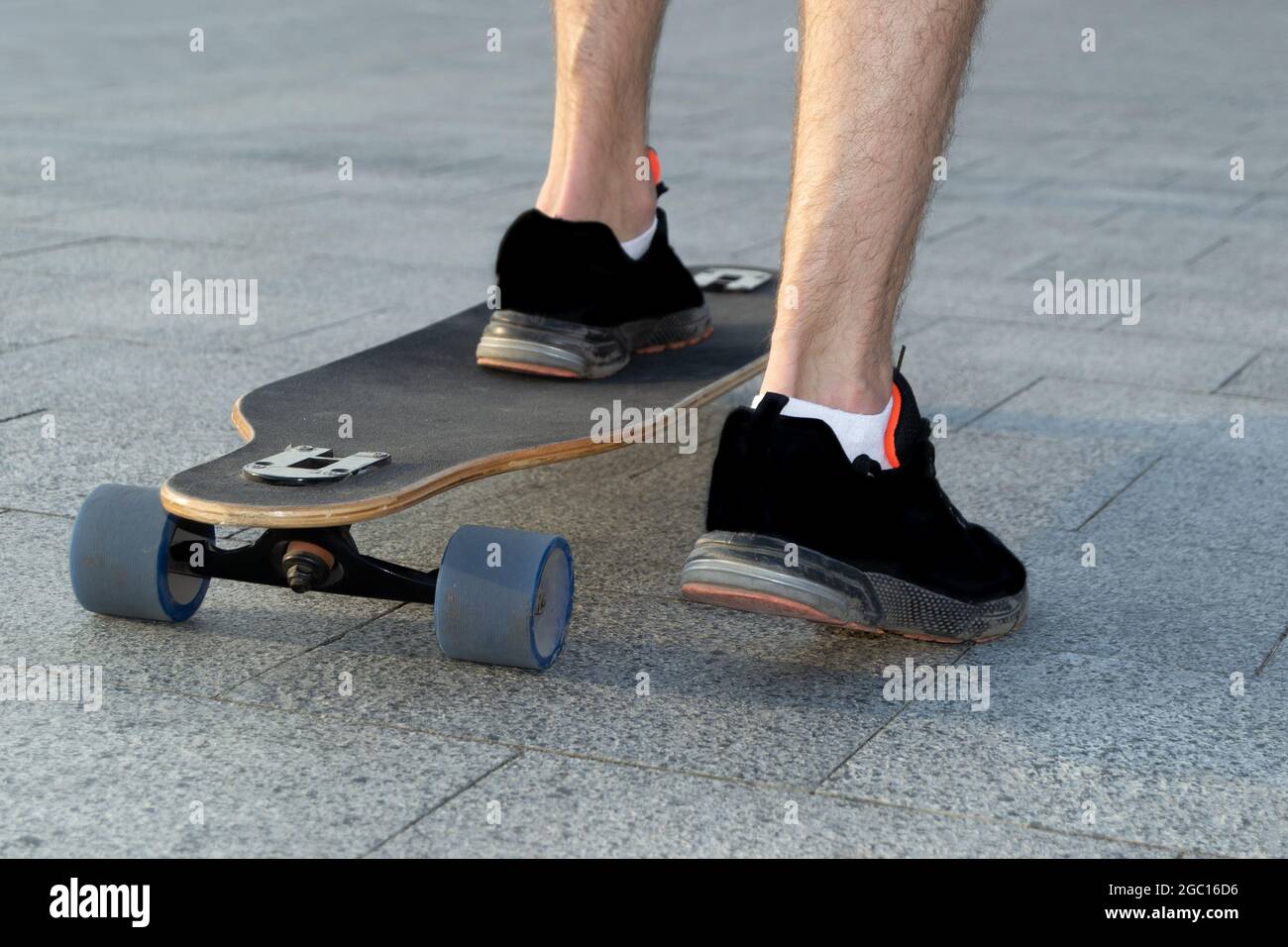 Primo piano delle gambe dello skater in sneakers nere su uno skateboard in un parco di cemento Foto Stock