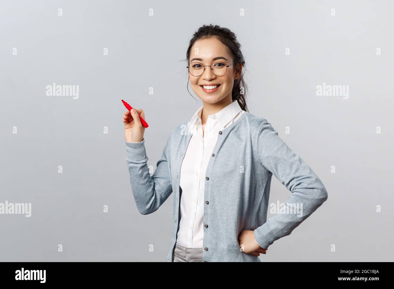 Insegnamento, educazione online e concetto di stile di vita. Giovane donna intelligente dipendente scrivere i suoi suggerimenti sulla lavagna, tenendo la penna e sorridendo Foto Stock