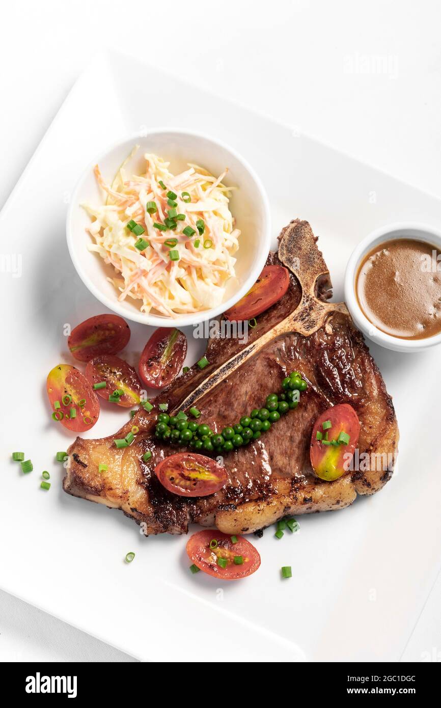 Bistecca di pepe verde di manzo T-bone alla griglia con insalata di cavolo e sugo su fondo piatto bianco Foto Stock