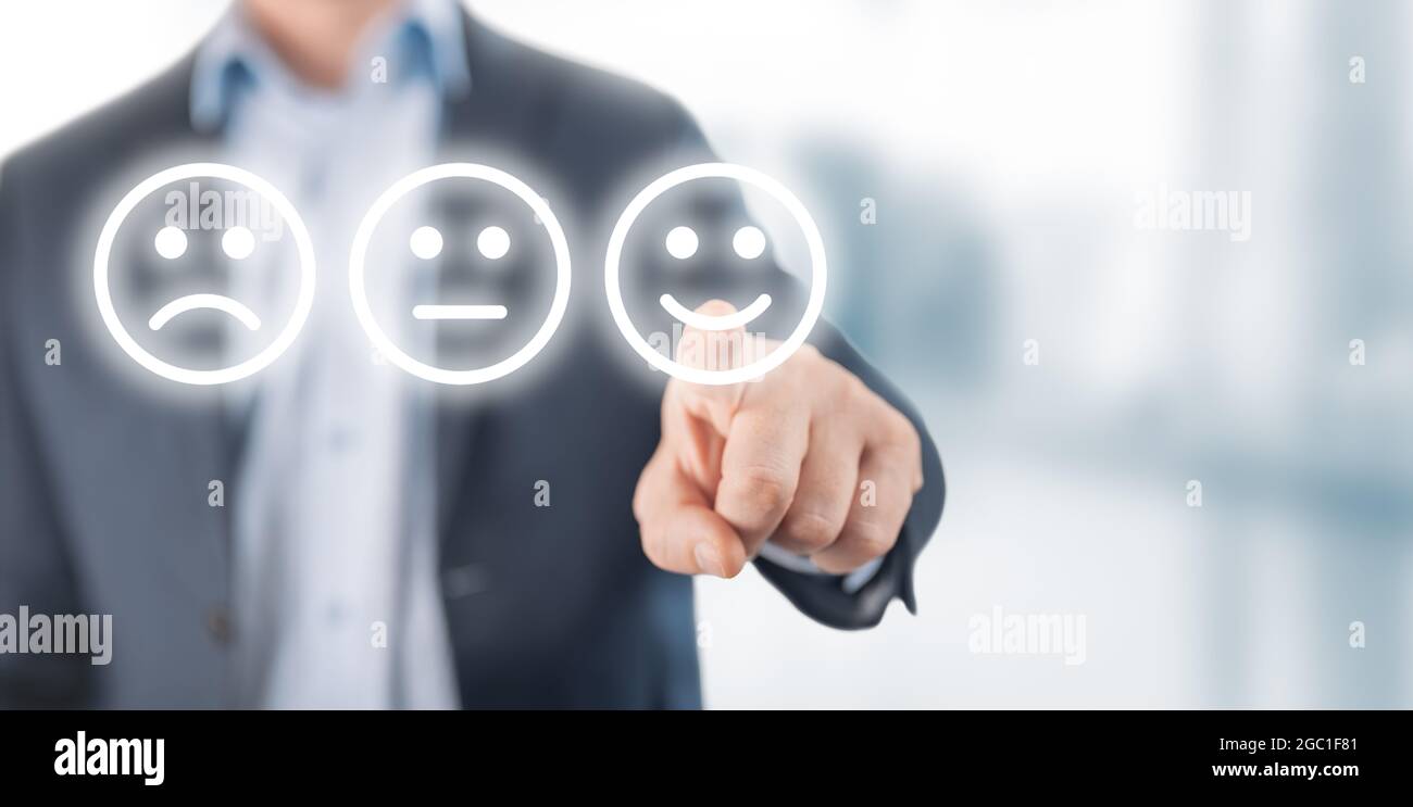 Valutazione concetto. Uomo che sceglie felice sorriso faccia emozione su sfondo sfocato. Mano di uomo d'affari che punta l'icona del volto sorridente dallo schermo come tassa positiva Foto Stock