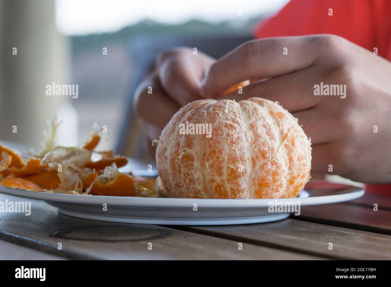 Primo piano di un mandarino pelato con le mani sullo sfondo. Foto Stock