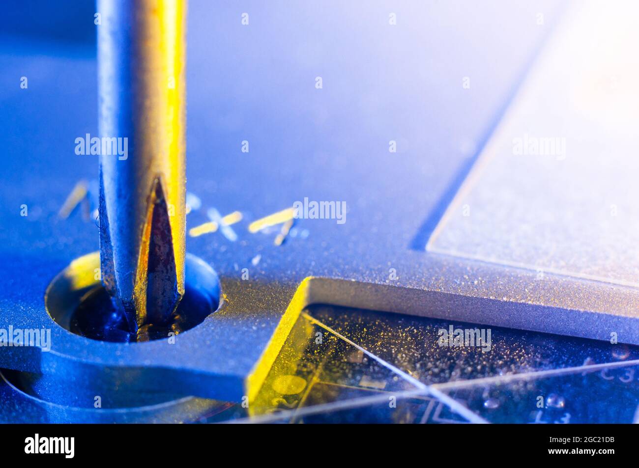 Svitando una piccola vite con un cacciavite Phillips in primo piano dalla custodia di un computer portatile, illuminazione giallo-blu Foto Stock