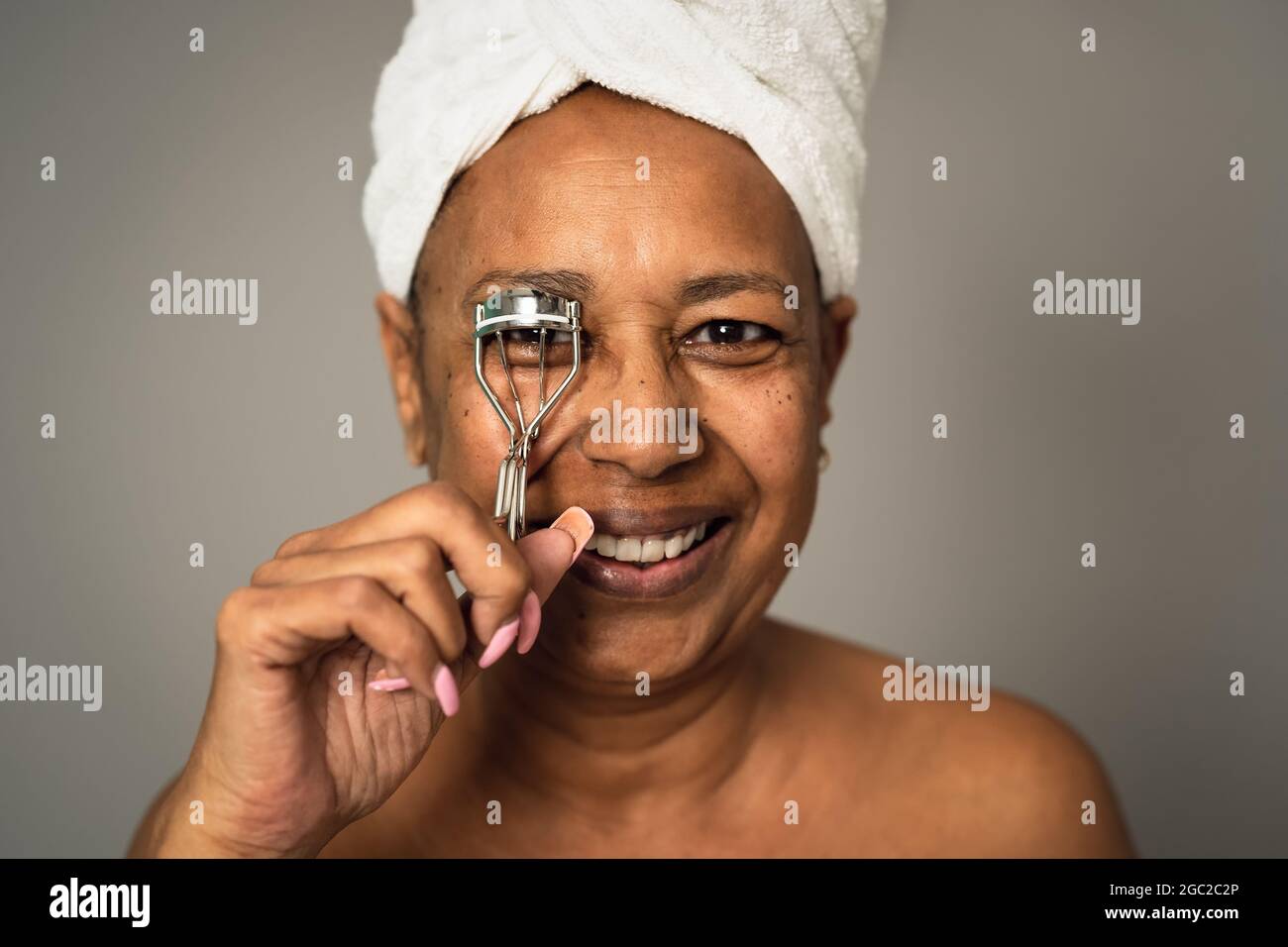 Donna anziana africana felice che usa l'arricciacapelli - concetto di stile di vita di bellezza e benessere della gente Foto Stock