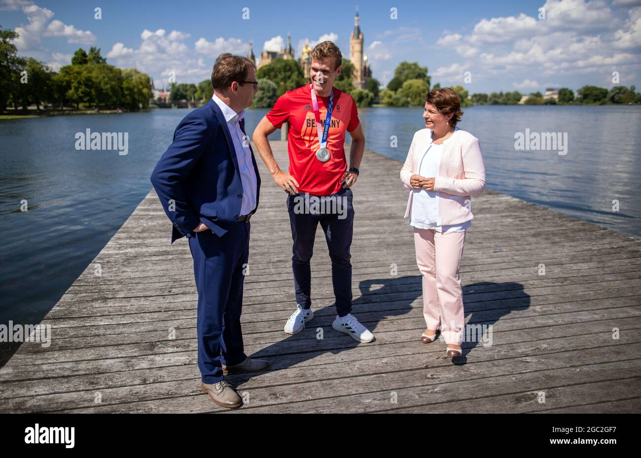 Schwerin, Germania. 06 agosto 2021. Hannes Ocik, colpo nella canottiera tedesca ai Giochi Olimpici di Tokyo, si trova tra Stefanie Drese (SPD), ministro degli Affari sociali del Meclemburgo-Vorpommern, e Torsten Renz (CDU), ministro degli interni del Meclemburgo-Vorpommern, di fronte al Castello di Schwerin. Ocik è stato accolto al club canottaggio Schwerin dopo il suo ritorno dal Giappone. Credit: Jens Büttner/dpa-Zentralbild/dpa/Alamy Live News Foto Stock