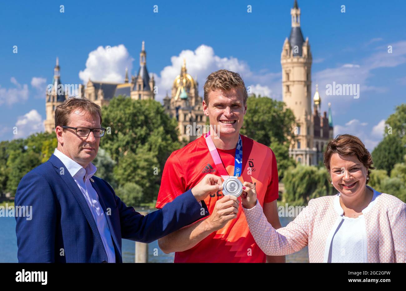 Schwerin, Germania. 06 agosto 2021. Hannes Ocik, colpo nella canottiera tedesca ai Giochi Olimpici di Tokyo, mostra la sua medaglia d'argento tra Stefanie Drese (SPD), ministro degli Affari sociali del Mecklenburg-Vorpommern, e Torsten Renz (CDU), ministro degli interni del Mecklenburg-Vorpommern, di fronte al Castello di Schwerin. Ocik è stato accolto al club canottaggio Schwerin dopo il suo ritorno dal Giappone. Credit: Jens Büttner/dpa-Zentralbild/dpa/Alamy Live News Foto Stock