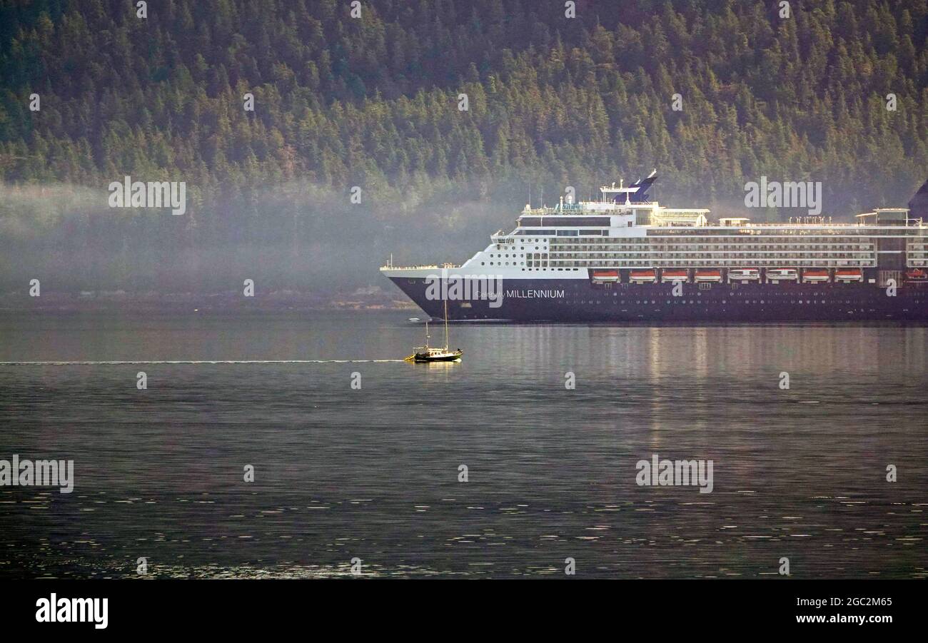 Alaska, Inside Passage, Pacific Coast; UNA gigantesca nave da crociera nana una piccola barca a vela mentre si muove lentamente a nord, attraverso la nebbia che sale da Baranof Island nella mattina presto lungo la costa occidentale dell'Alaska sul passaggio interno. Foto Stock