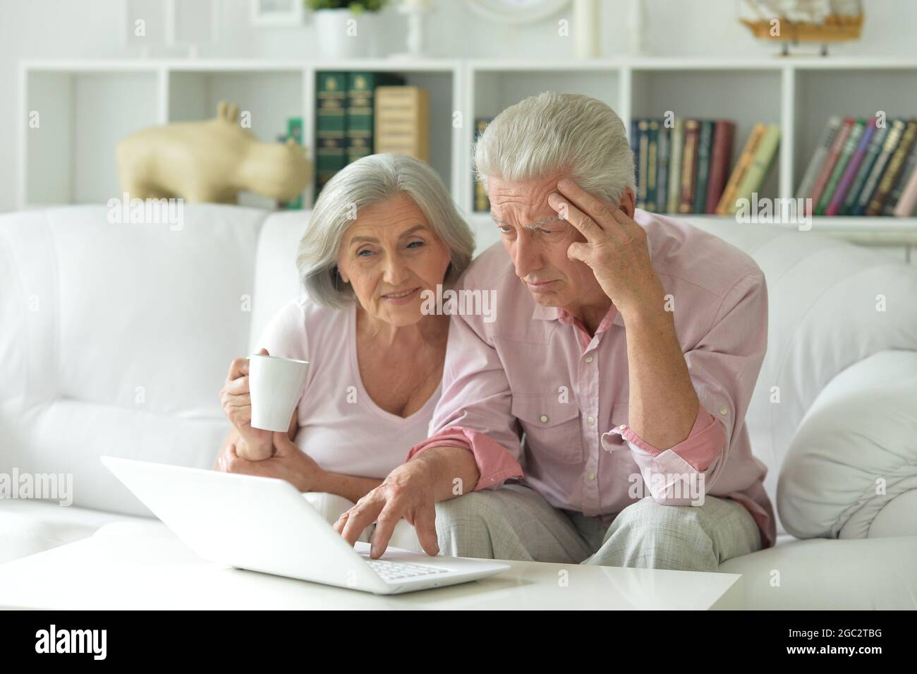 Due anziani seduti sul divano con computer portatile Foto Stock