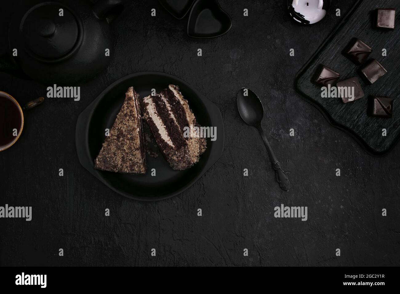 Pezzi di torta su un piatto nero, tè con dolci su sfondo scuro. Disposizione piatta Foto Stock