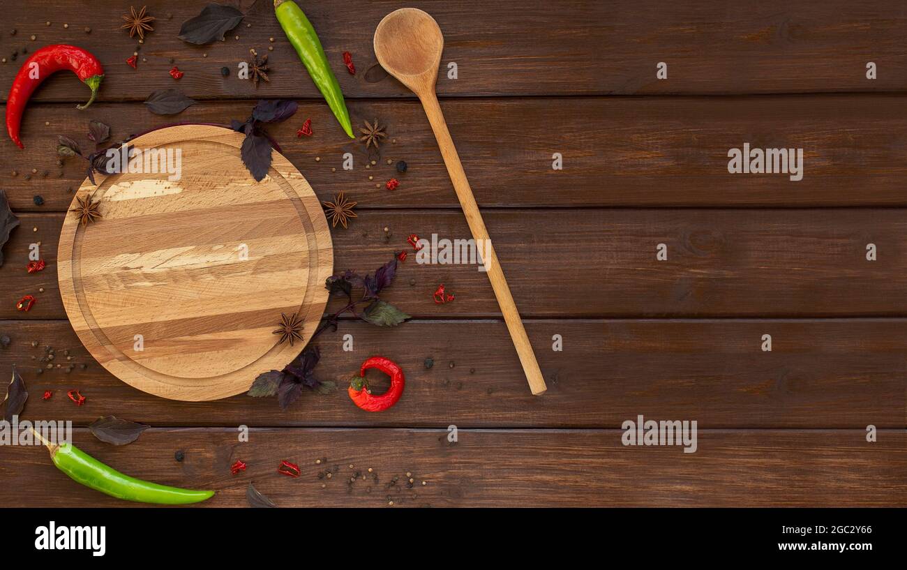 Piatto rotondo di legno fatto a mano e cucchiaio con spezie, pepe, foglie di basilico e anice su fondo di legno marrone. Vista dall'alto, disposizione piatta, spazio per la copia Foto Stock