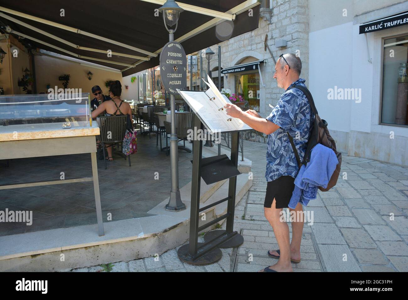 Porec, Croazia - 10 luglio 2021. Un turista guarda un menu all'esterno di un ristorante nel centro storico della città costiera medievale di Porec in Istria Foto Stock