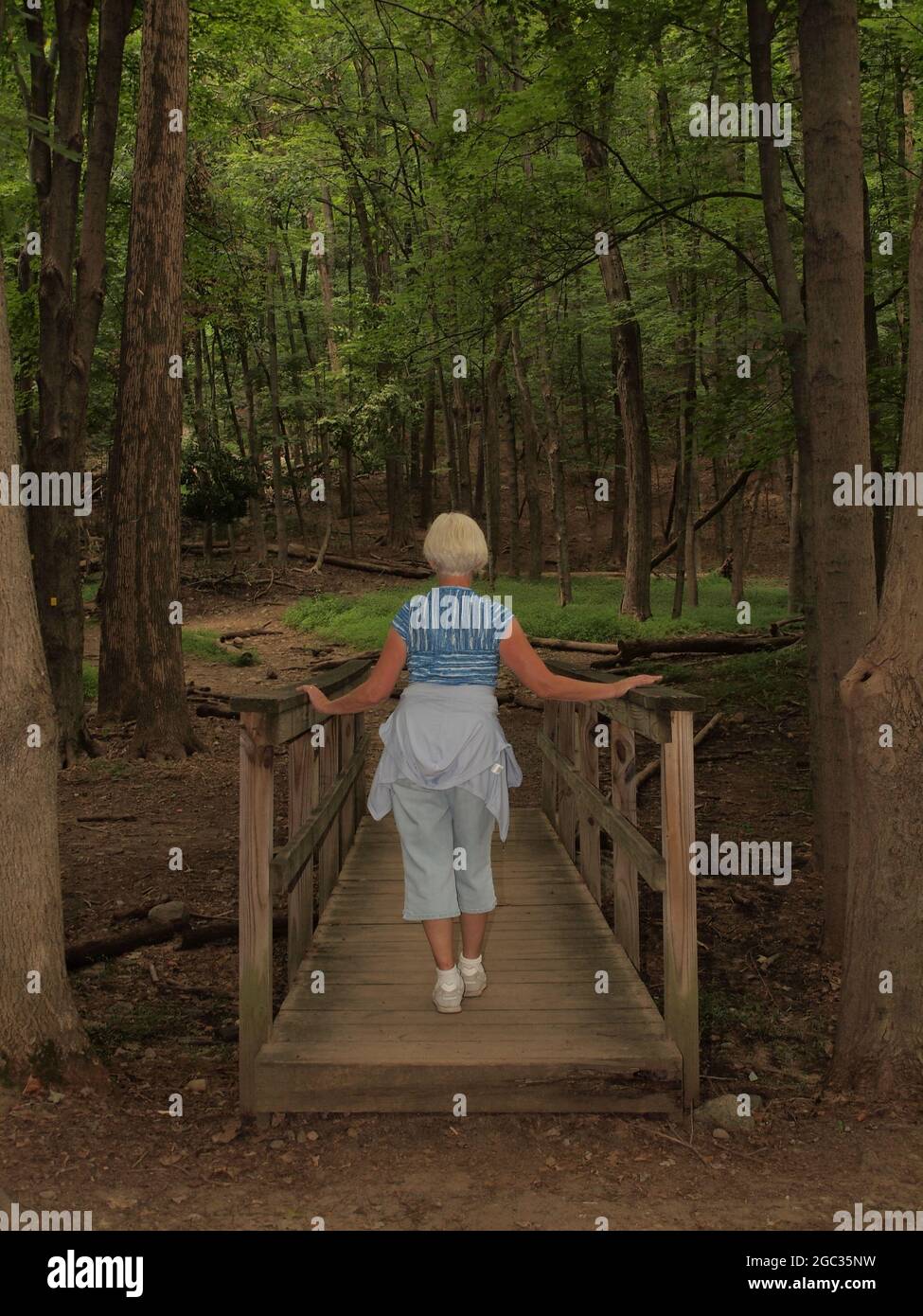 Donna bionda passeggiando lungo un piccolo ponte di legno in un parco della contea locale in New Jersey ottenere esercizio. Ramapo prenotazione in New Jersey. Foto Stock