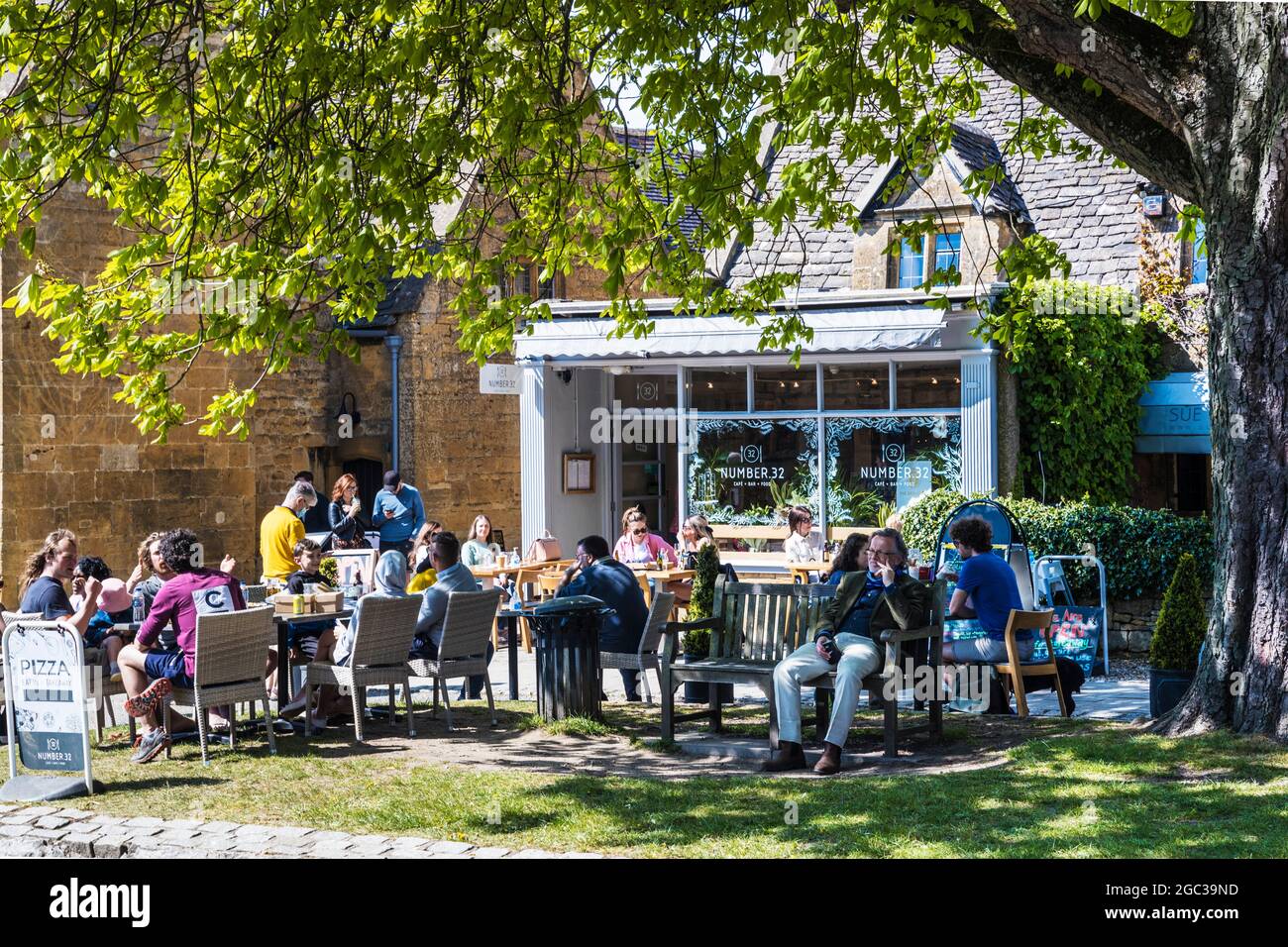 La gente gode del sole primaverile, fuori da un caffè nella città di Cotswold di Broadway nel Worcestershire. Foto Stock