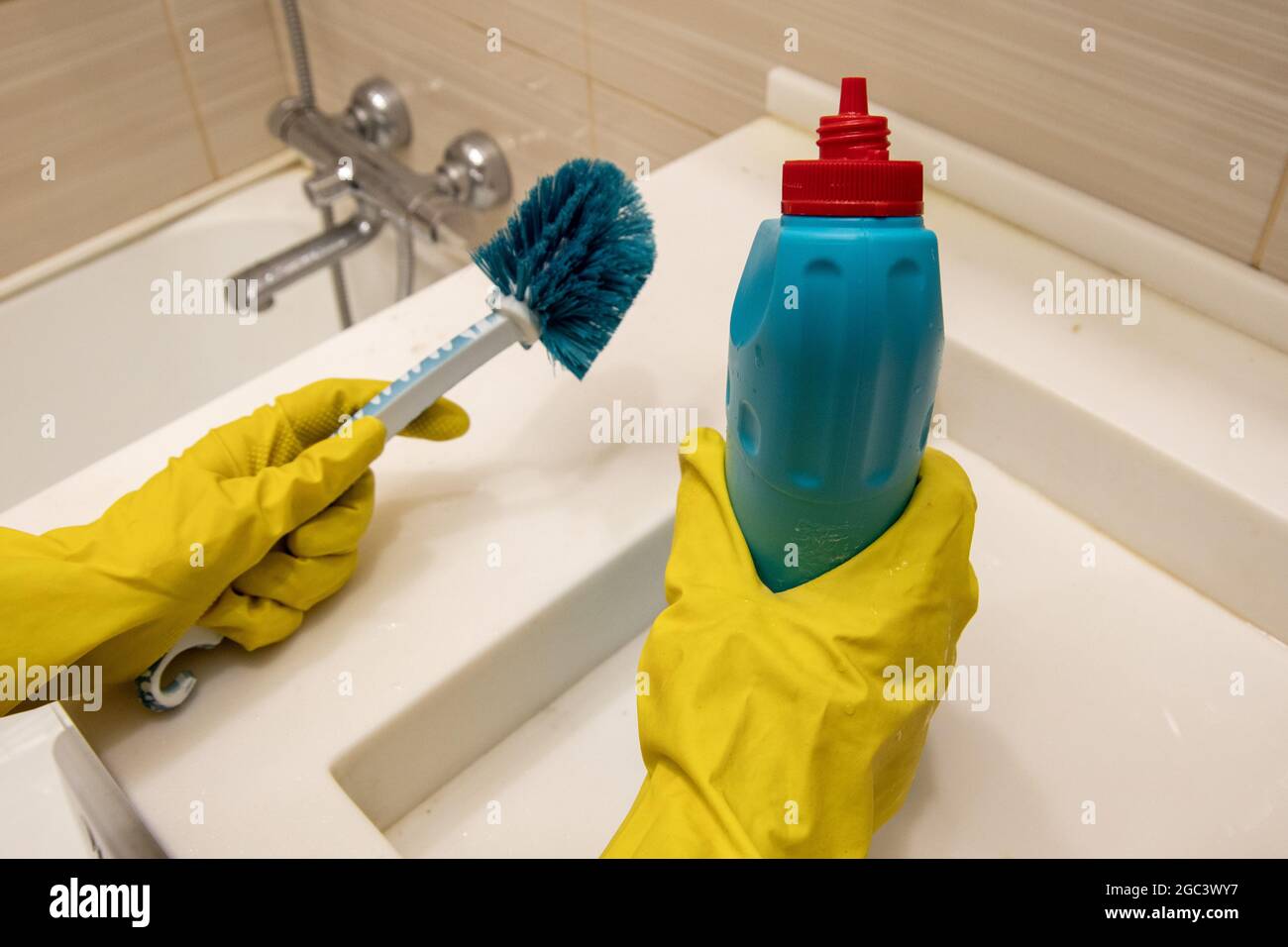 Le mani in guanti gialli tengono il detergente e la spugna blu  sull'impugnatura per pulire il bagno. Il concetto di lavoro a casa,  disinfezione Foto stock - Alamy