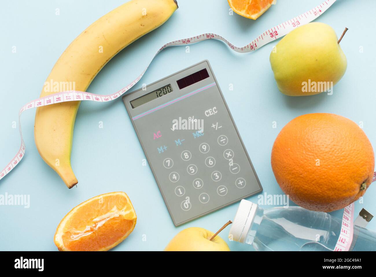 Calcolatrice con numeri 1200, bottiglia d'acqua, metro a nastro e frutta su sfondo blu. Concetto di alimentazione sana - calcola l'assunzione di alimentazione quotidiana Foto Stock