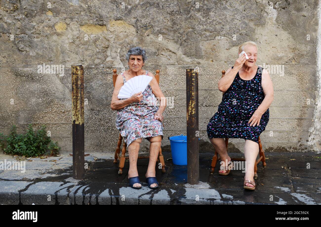 Luglio 2015, Napoli Italia. Anziane donne italiane che si siedono fuori sulla strada con un secchio d'acqua per aiutare con il calore bruciante. Foto Stock