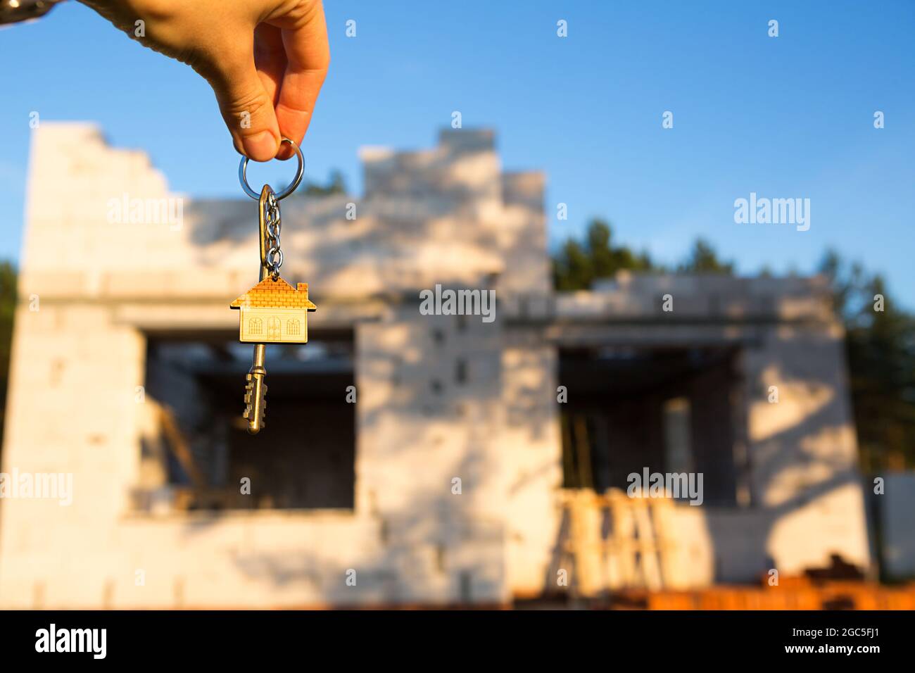 Mano con la chiave per la futura casa sullo sfondo di un cantiere e pareti in cemento poroso blocco. Costruire una casa, spostandosi ad un n Foto Stock