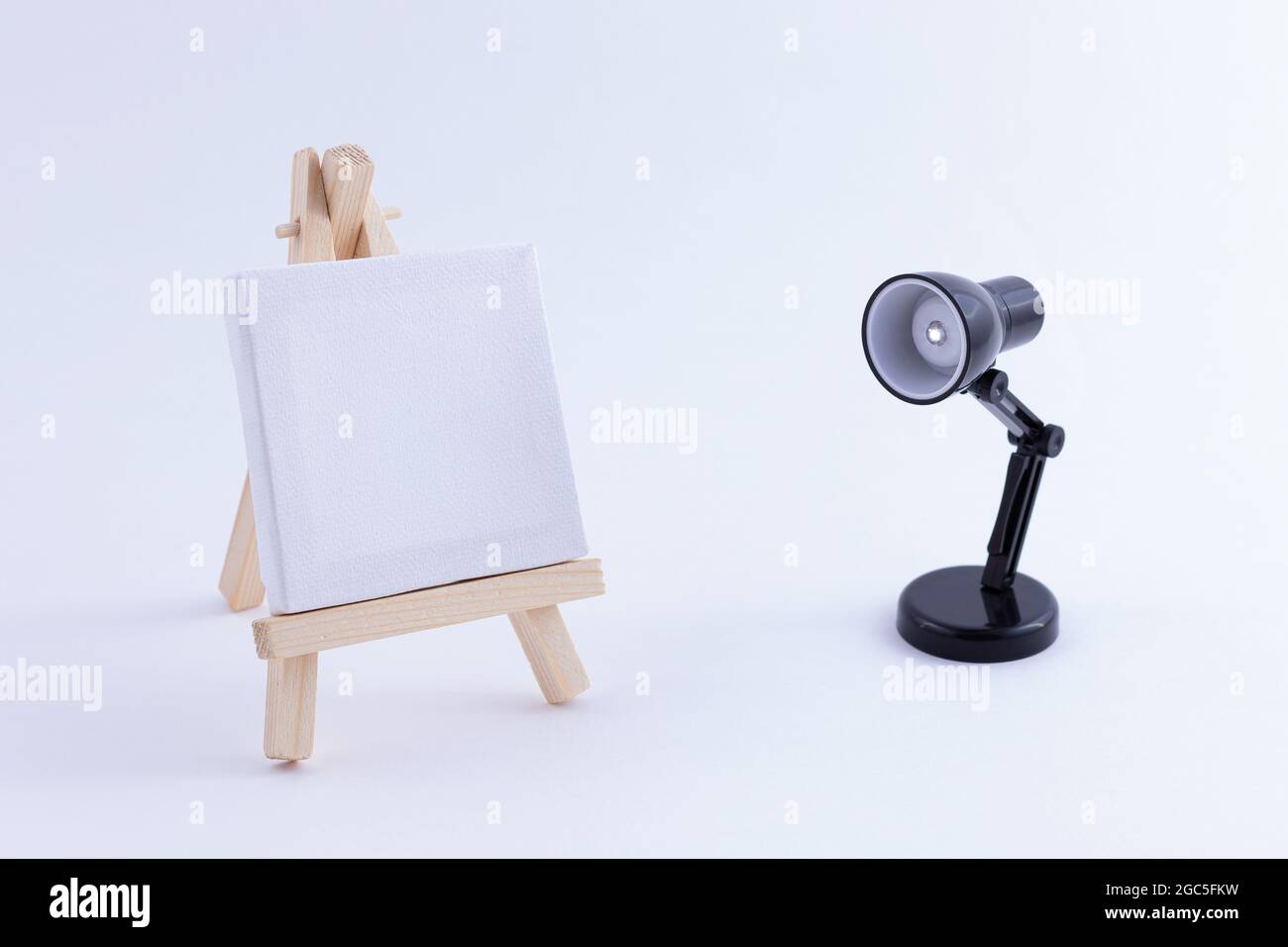 Easel in legno in miniatura con tela bianca quadrata vuota per artisti e  pittori - Mockup. Mini supporto in legno con tavola da disegno pulita e  piccola lampada da tavolo nera su