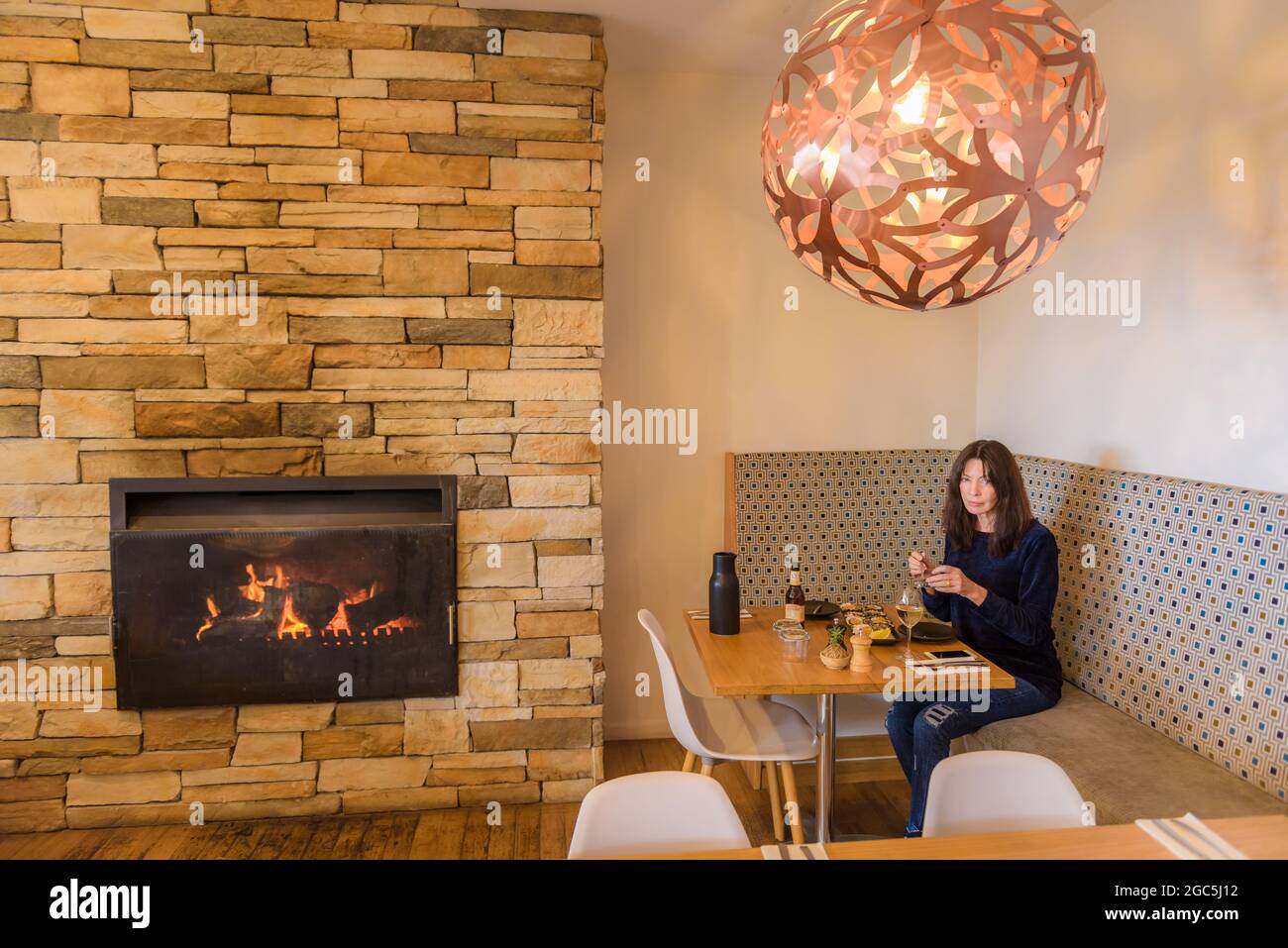 Una turista femminile si siede in un alcova vicino ad un caminetto acceso gustando il pranzo al ristorante 1802 a Coffin Bay, Penisola Eyre, nell'Australia Meridionale. Foto Stock