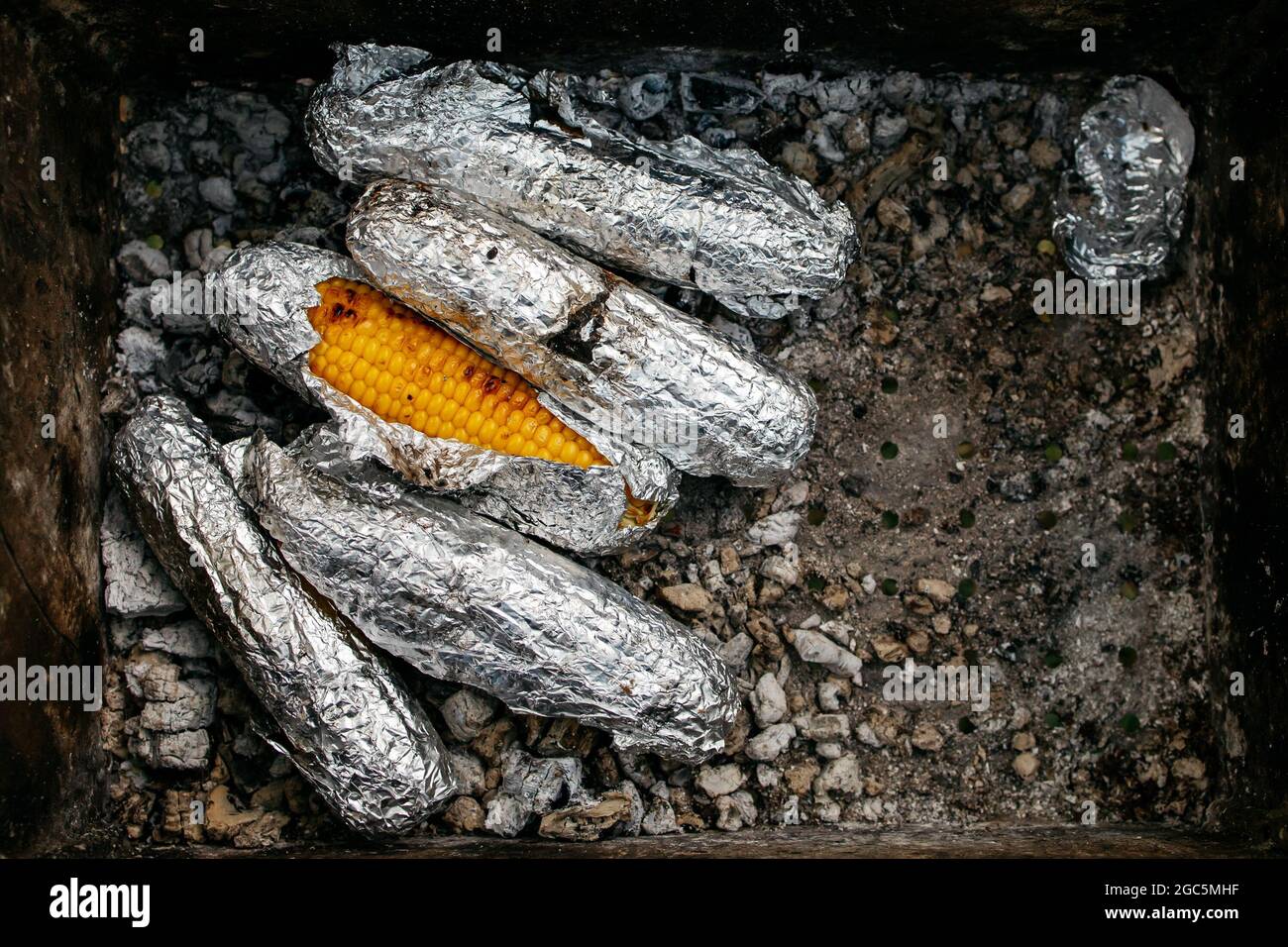 Mais dolce grigliato nel fuoco. Verdure cooccate in un foglio di alluminio all'aperto. Foto creativa. Foto Stock