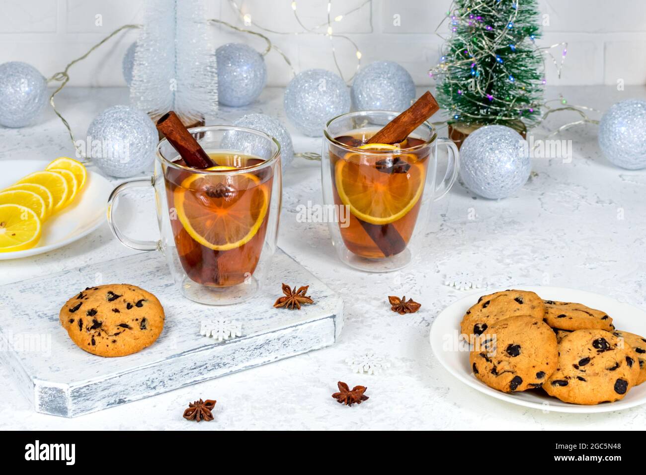 Due tazze di tè di vetro con limone, cannella e anice sullo sfondo del nuovo anno interno con ghirlande, palle e artificiale Foto Stock