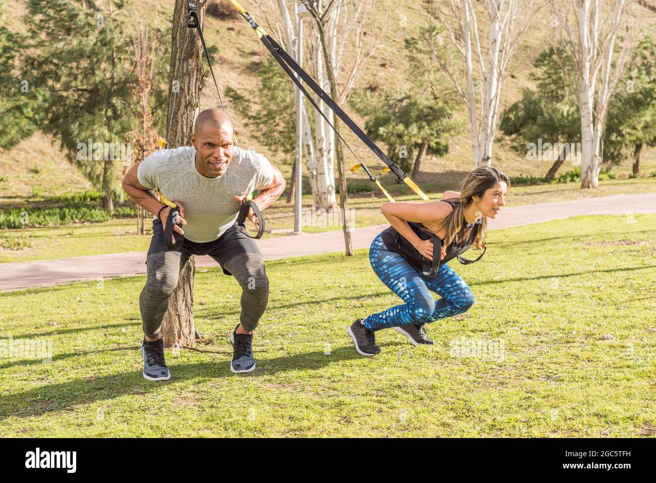 I partner atletici che fanno esercizi di schiena squatting con cinghie fitness nel parco Foto Stock