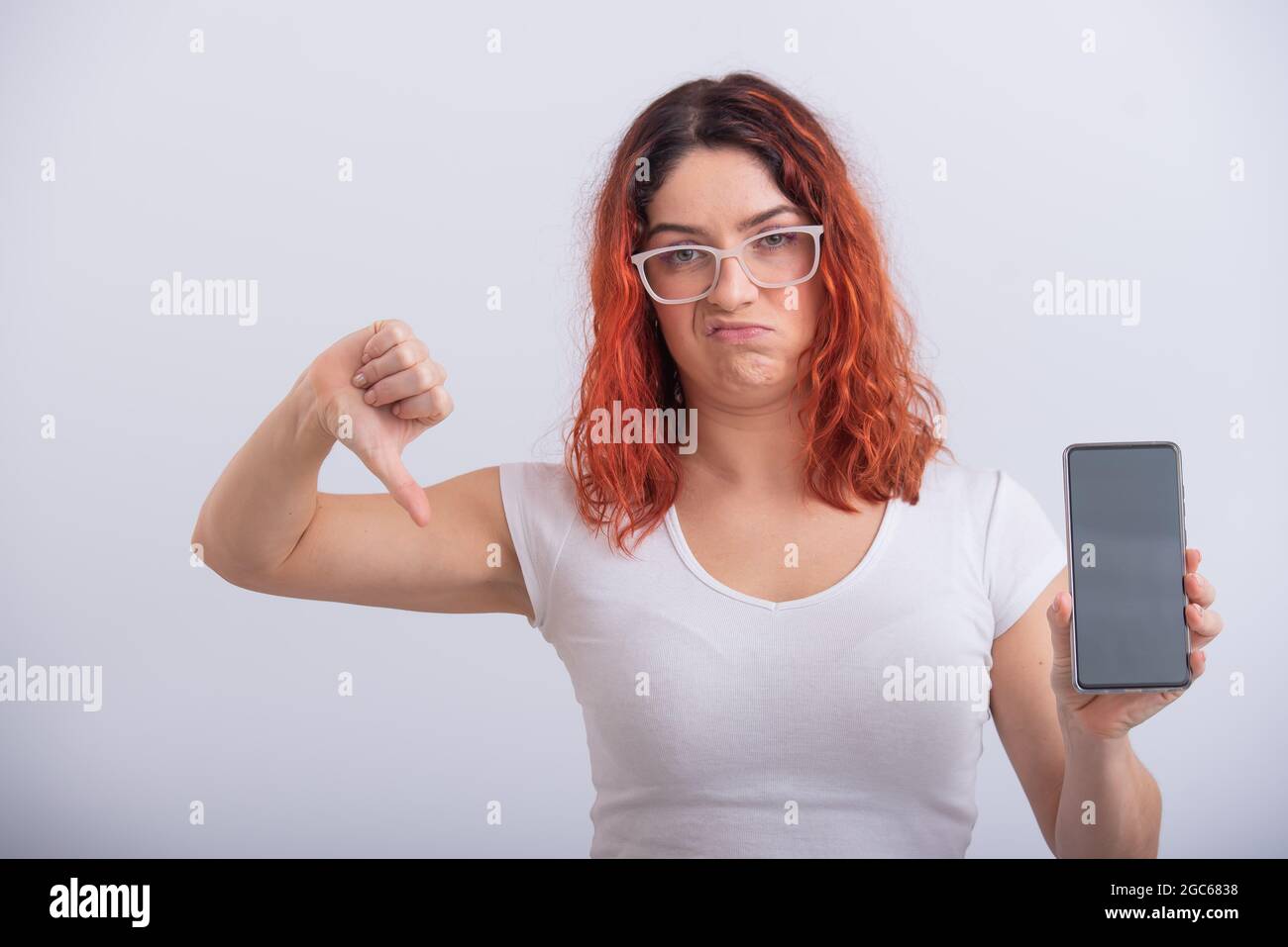 Donna caucasica che tiene uno smartphone con schermo nero e mostra il pollice verso il basso. Foto Stock