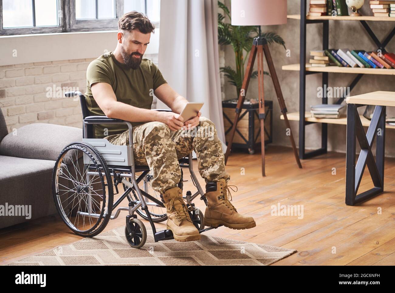 Giovane veterano seduto su una sedia a rotelle e utilizzando un computer tablet Foto Stock