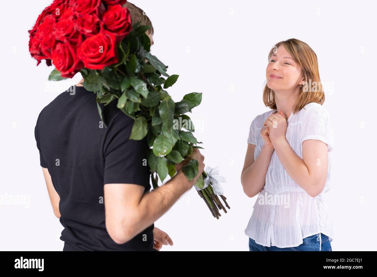 L'uomo di consegna in t-shirt nera che tiene un bouquet enorme delle rose sulla spalla per la giovane donna graziosa sorridente e soddisfatto per Foto Stock