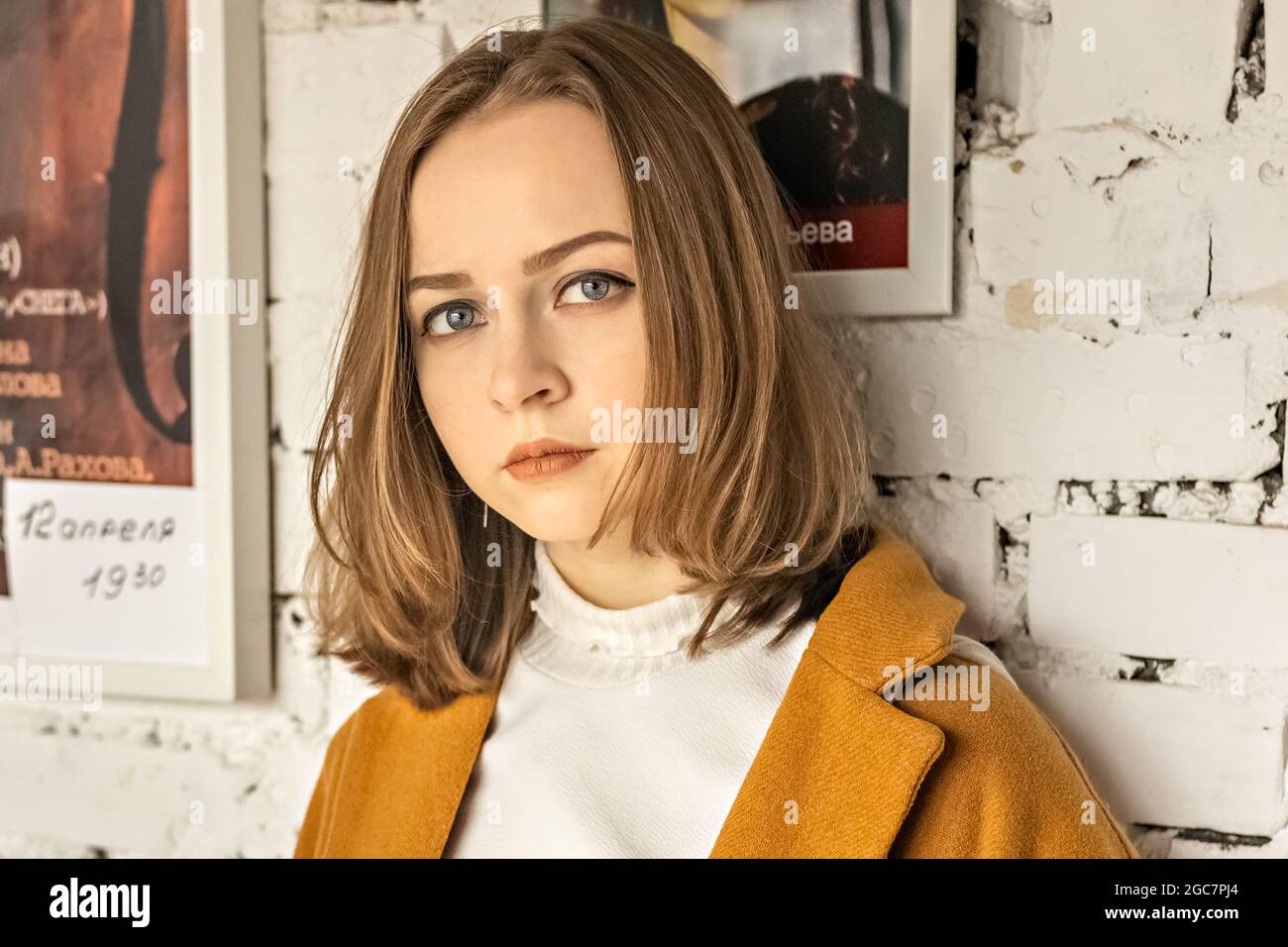 Ritratto di una giovane adolescente contro una parete bianca di mattoni con un poster. Foto Stock