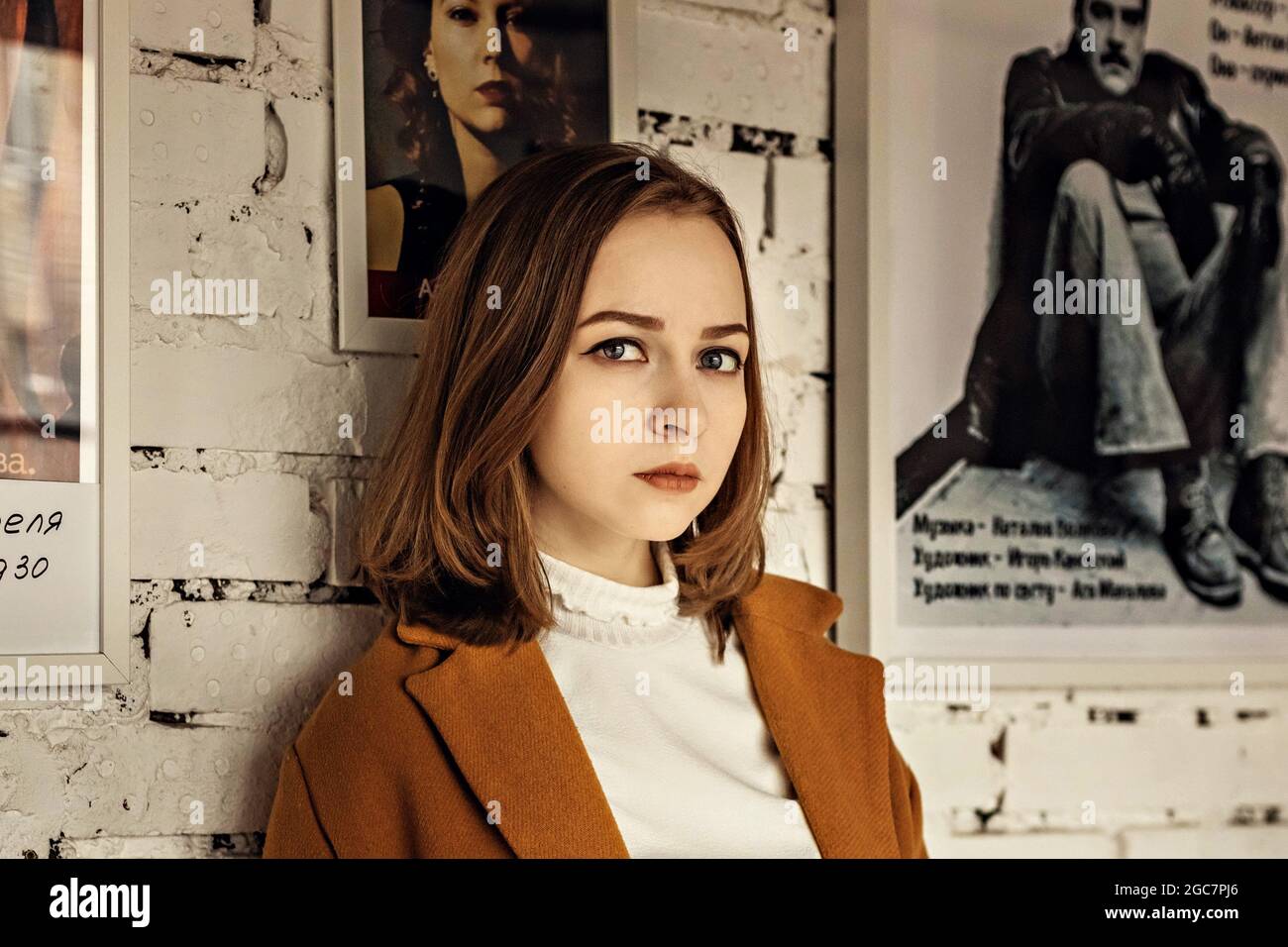 Ritratto di una giovane adolescente contro una parete bianca di mattoni con un poster. Foto Stock