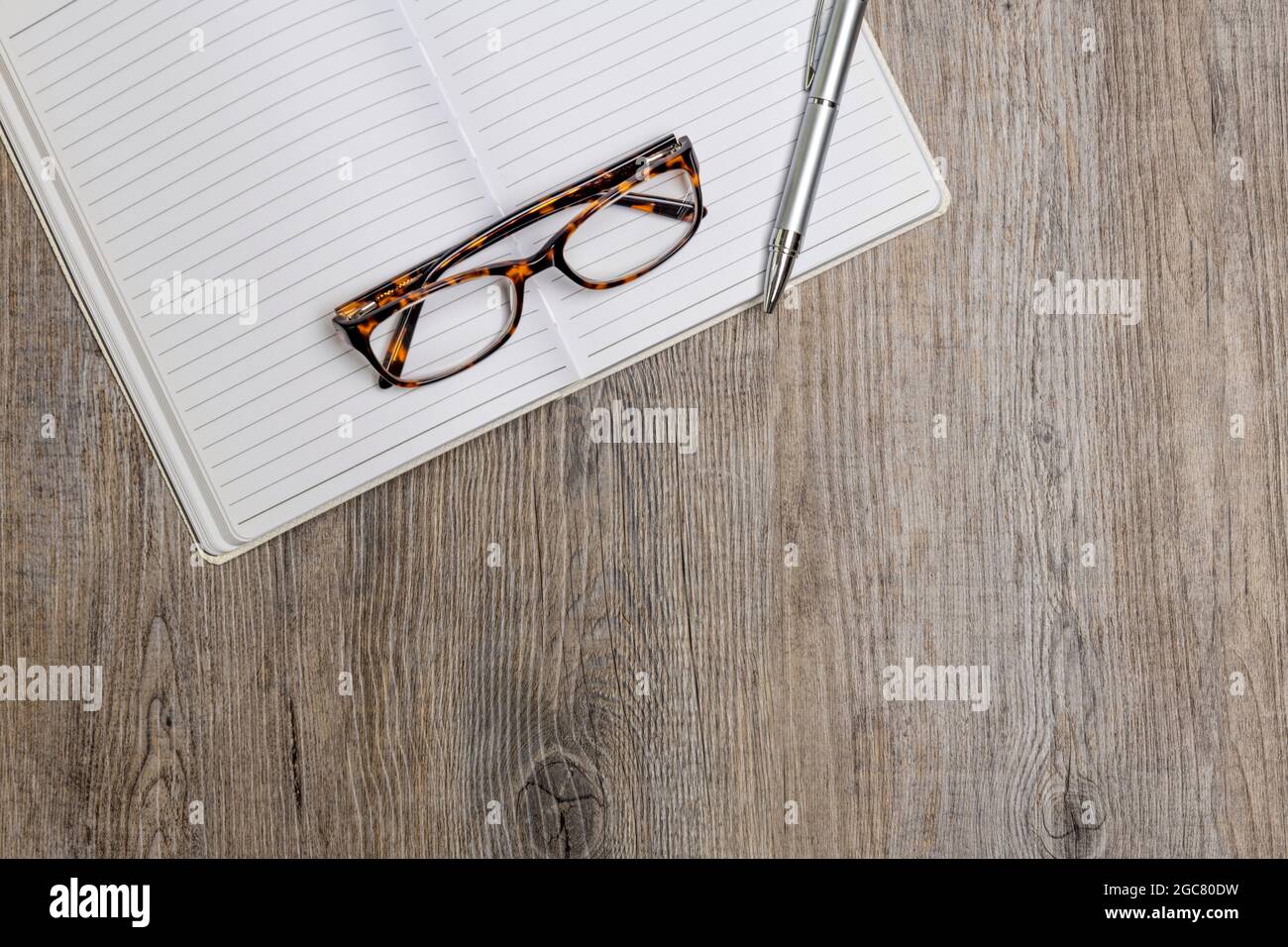 penna e occhiali sopra un notebook su una superficie di legno. Disposizione piatta. Foto Stock