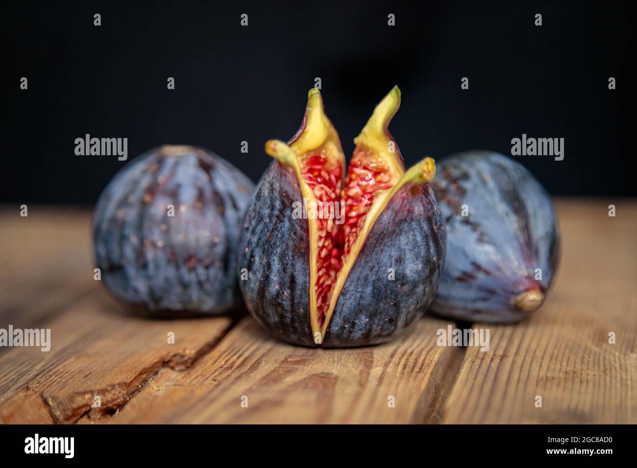 Fichi porpora appena tagliati su sfondo di legno da vecchie tavole. Fichi esotici grezzi. Tasto basso Foto Stock