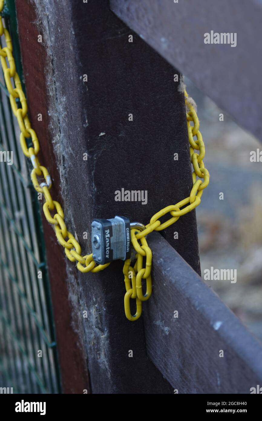 Un lucchetto che blocca l'ingresso a una strada privata in una fattoria dove vogliono che altri si tengano fuori e vedere la catena gialla intorno al cancello e l'area recintata Foto Stock