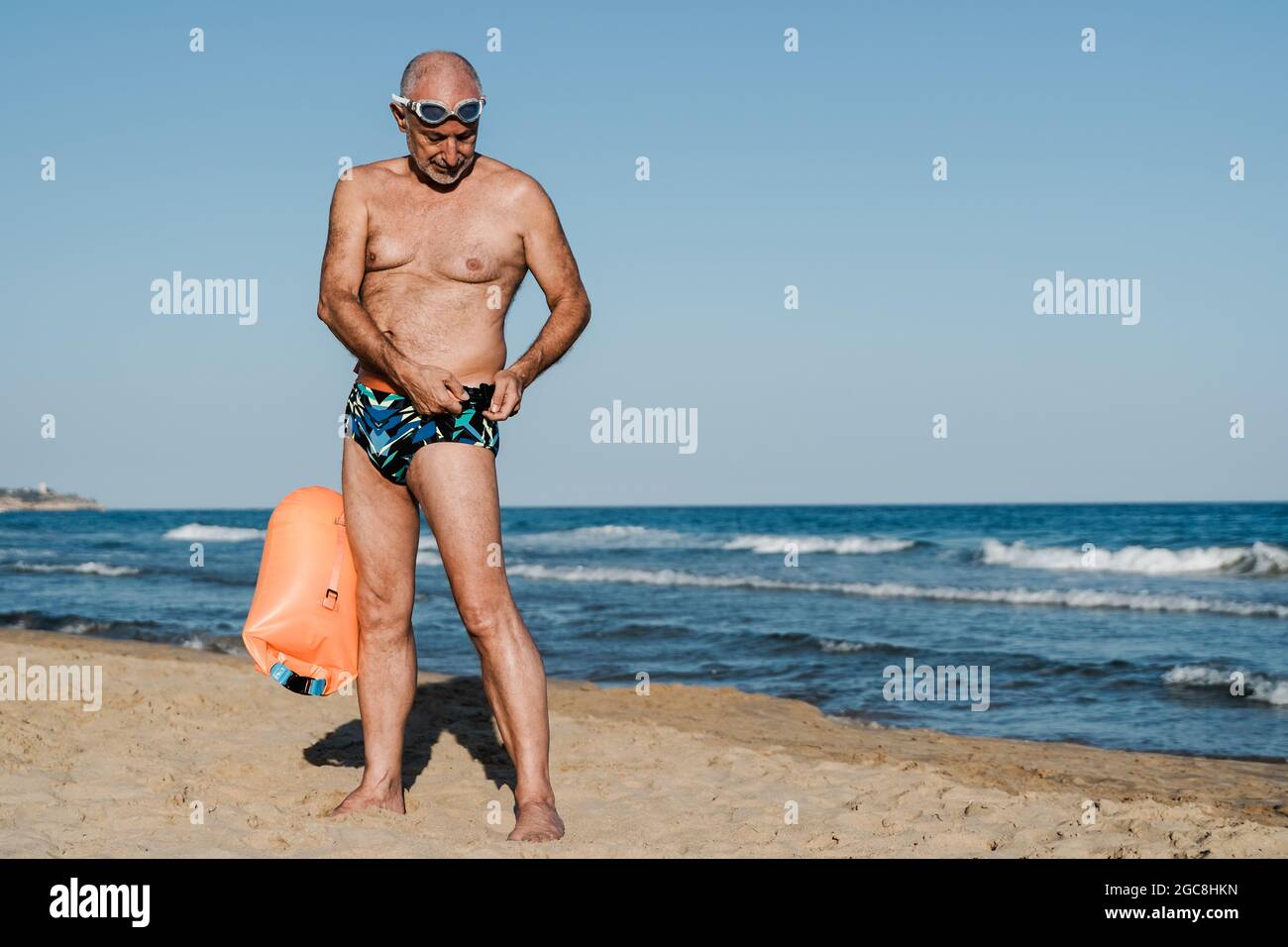 Sport nuotatore senior uomo formazione per nuotare in mare aperto triathlon con spiaggia sullo sfondo - anziani e stile di vita sano Foto Stock