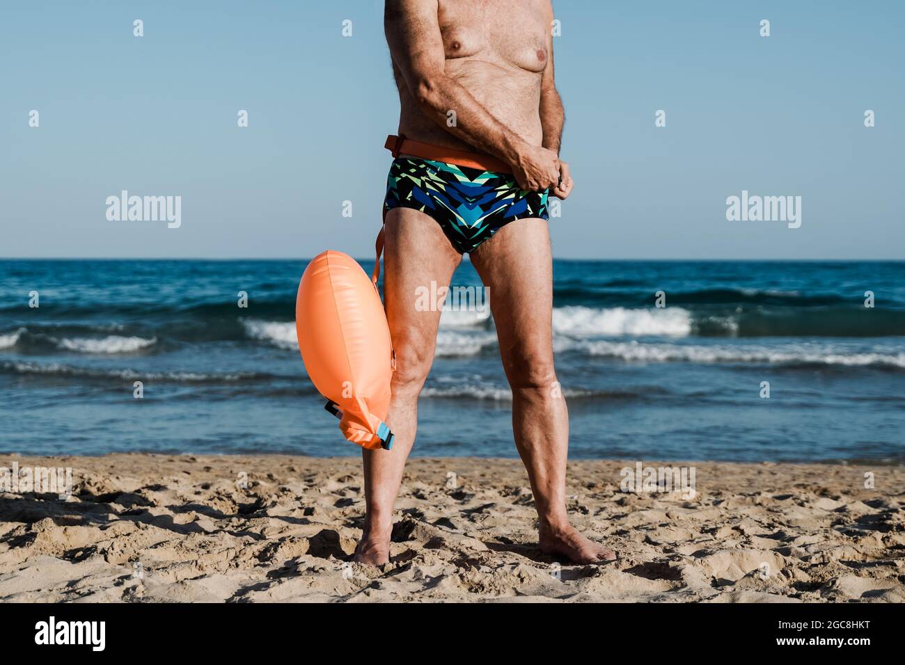 Sport nuotatore senior uomo formazione per nuotare in mare aperto triathlon con spiaggia sullo sfondo - anziani e stile di vita sano Foto Stock