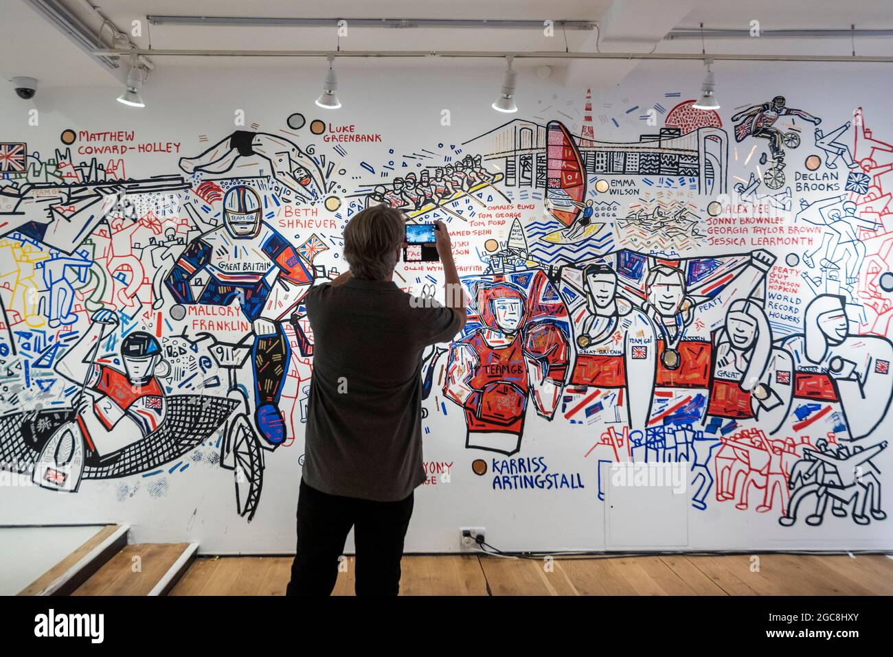 Londra, Regno Unito. 7 agosto 2021. Un visitatore vede il murale di ben Mosley incentrato sul successo degli atleti del Team Great Britain (GB) alle Olimpiadi di Tokyo 2020. Basato al pop-up Team GB Studio di Carnaby Street, l'artista aggiorna il suo murale quotidiano con i successi degli atleti. Gli eventi dell'ultimo giorno e la cerimonia di chiusura sono gli unici lavori rimasti. Team GB è diventato il primo ad adottare gettoni non fungibili (NFT) con i risultati precedenti degli atleti, che possono essere acquistati attraverso un negozio dedicato. Credit: Stephen Chung / Alamy Live News Foto Stock