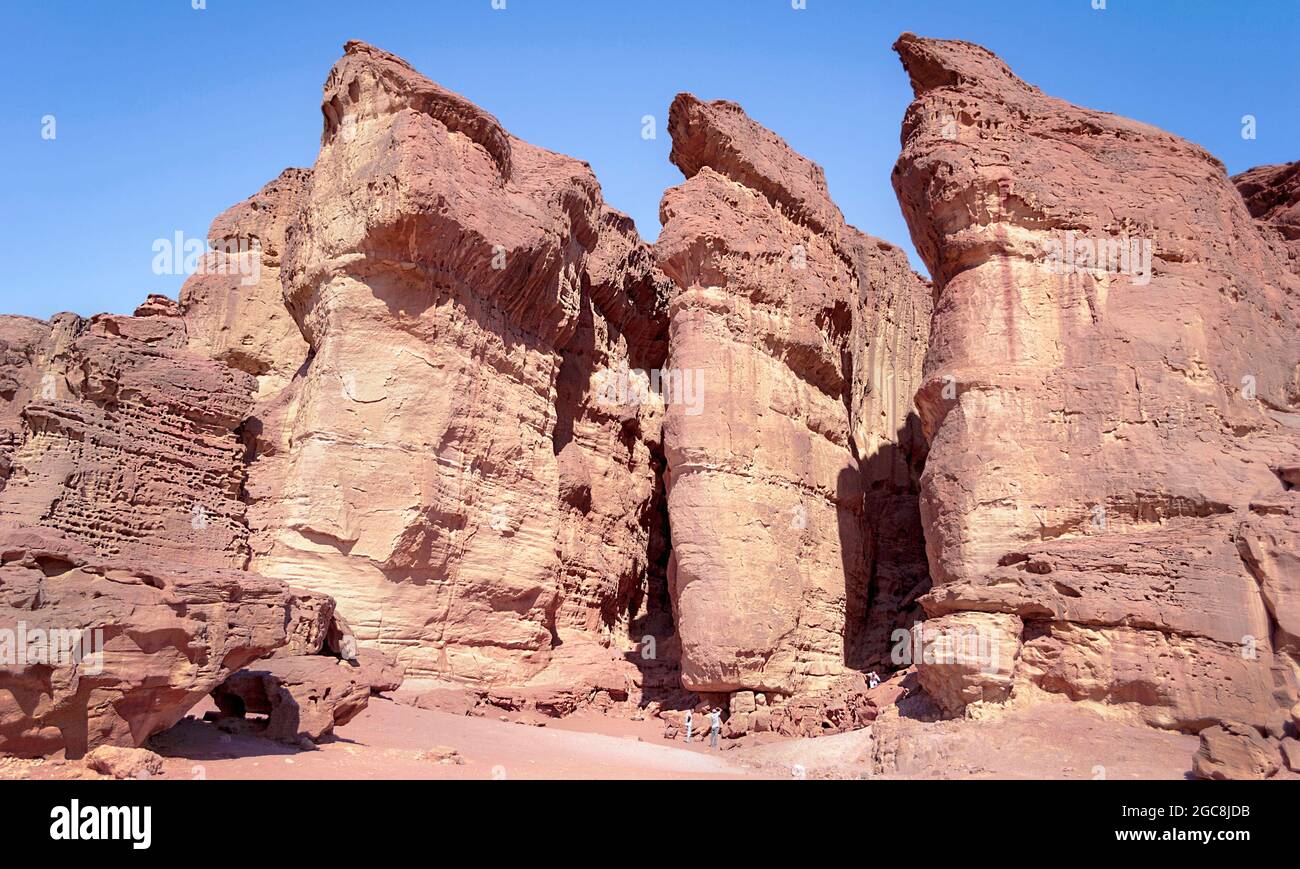 I piccoli turisti che guardano in su alla formazione maestosa di pietra arenaria dei pilastri di Solomons nel parco di Timna in Israele con uno sfondo blu chiaro del cielo Foto Stock