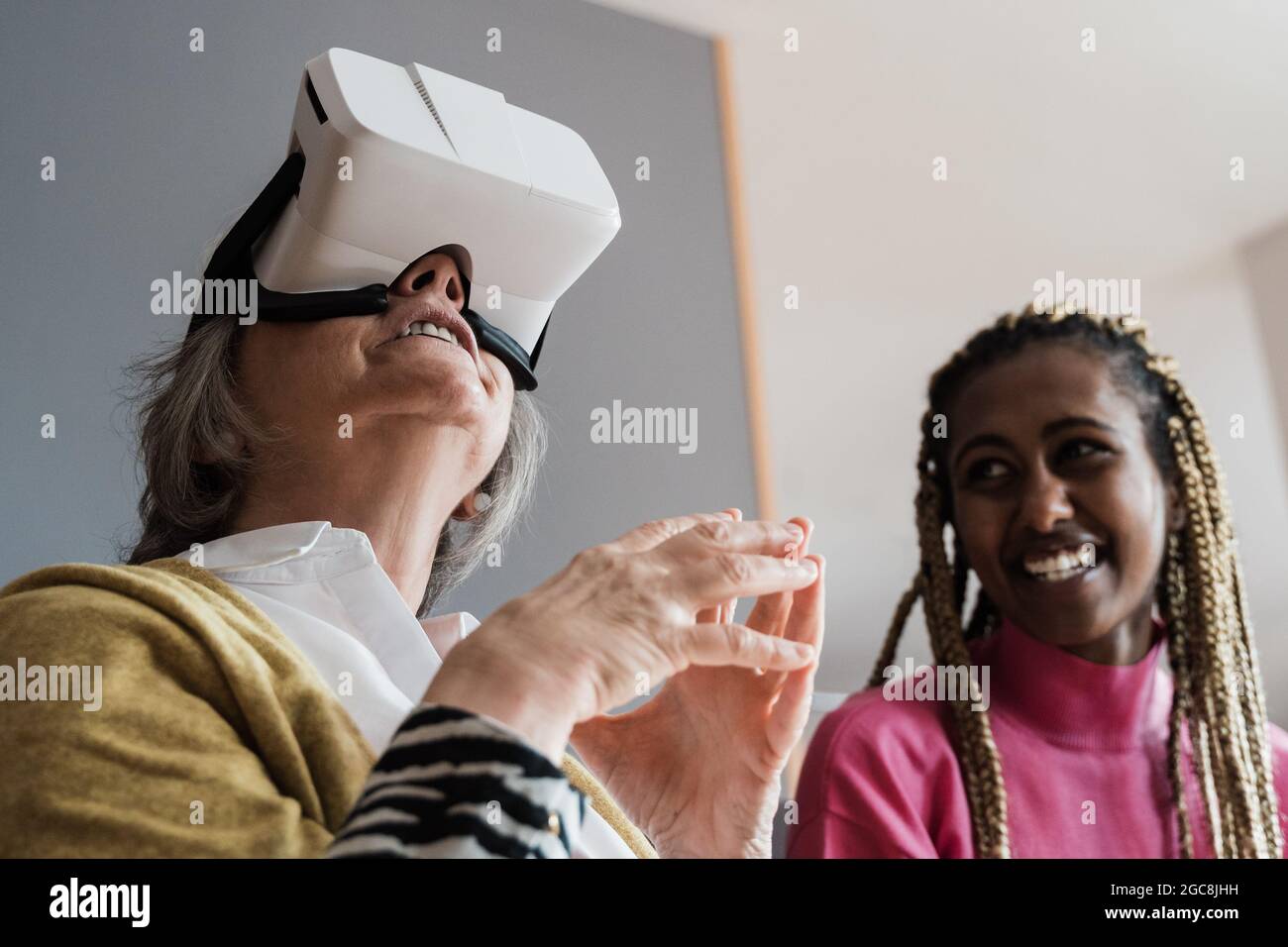 Persone multirazziali che utilizzano il visore per realtà virtuale in interni a casa - Focus sul volto della donna anziana Foto Stock